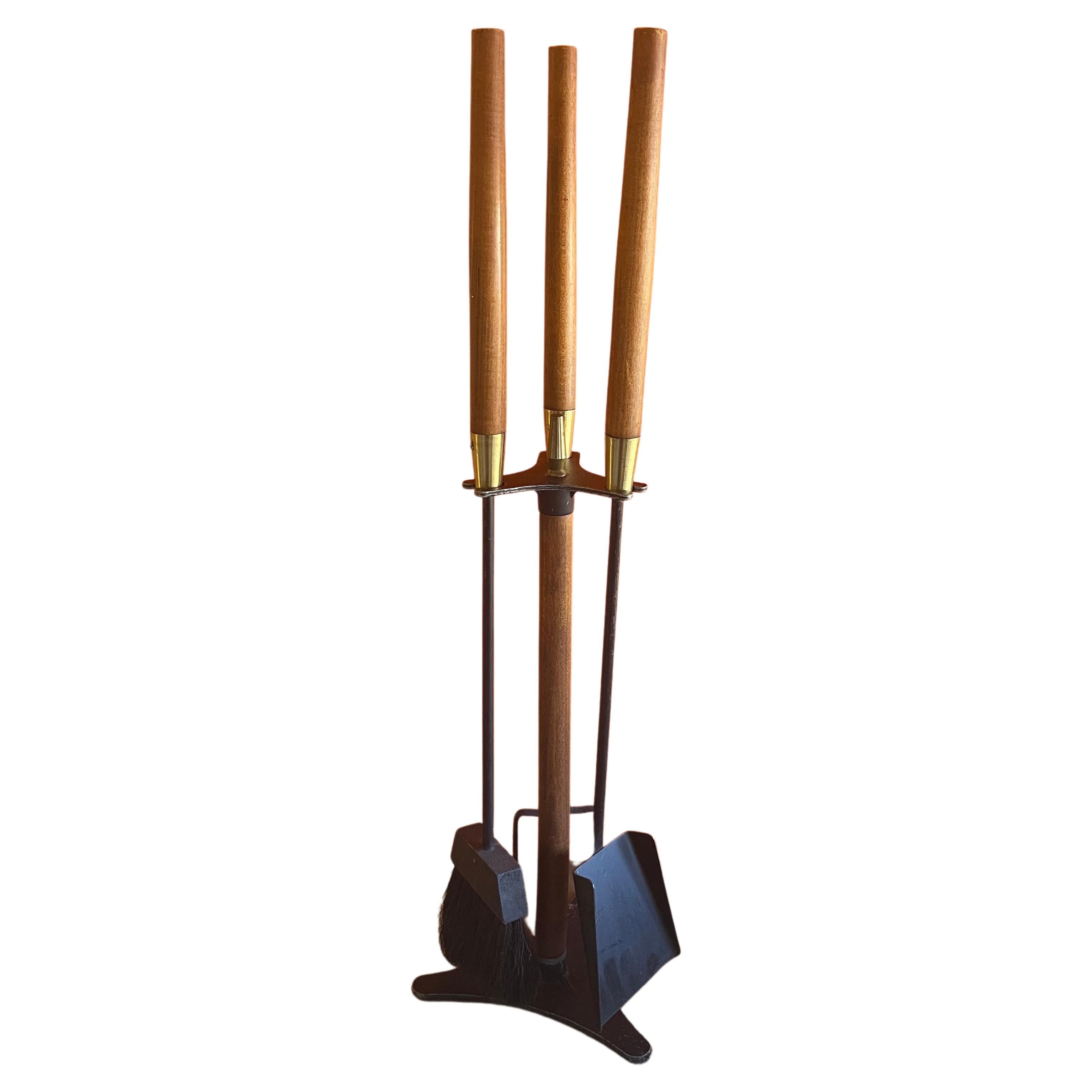Modernist MCM set of fire place tools in cast iron with brass fittings and walnut handles, circa 1970s. There are three tools (shovel, brush and poker) and a round brass stand in vintage condition. The set measures 32.75