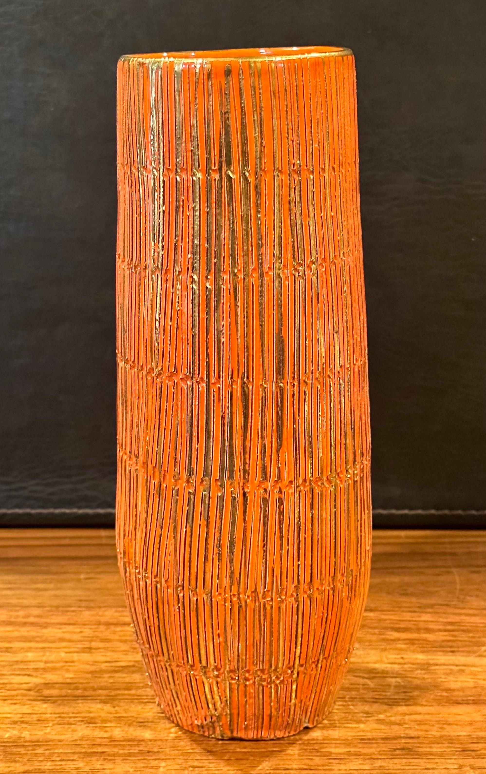 A vibrant orange glaze and gold gilt MCM Sgraffito ceramic vase by Aldo Londi for Bitossi Seta Series (silk), circa 1950s.  The vase is striated with bands incised with small uneven shapes. The gold gilt stripes have been hand painted over the