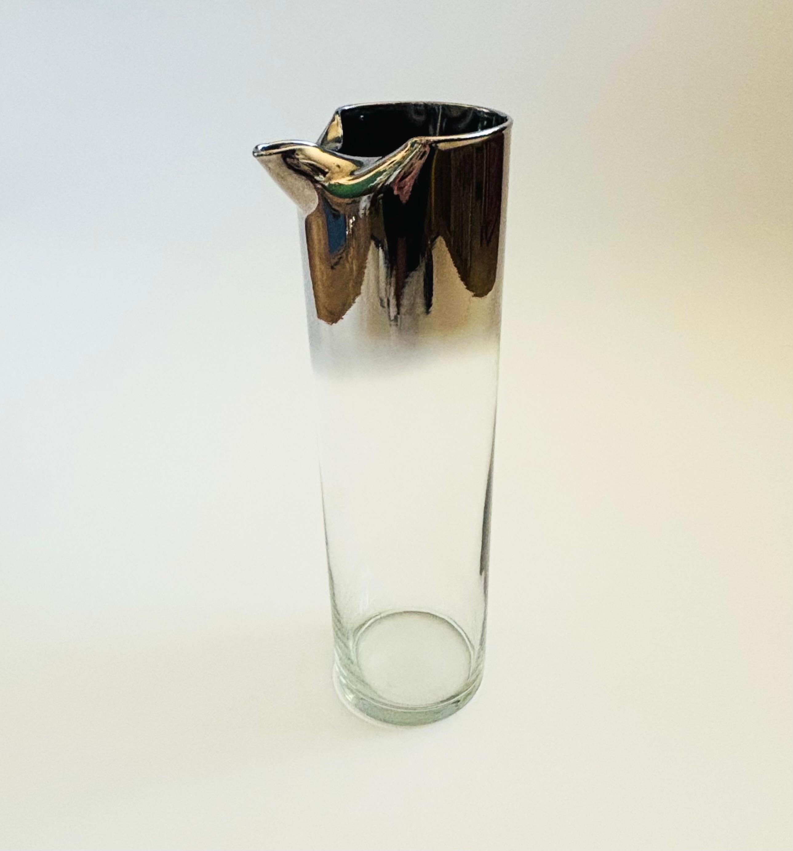 A mid century glass pitcher with silver fade finish to the top.. Nice modern cylinder shape with a spout formed into the top. Perfect for serving drinks.


