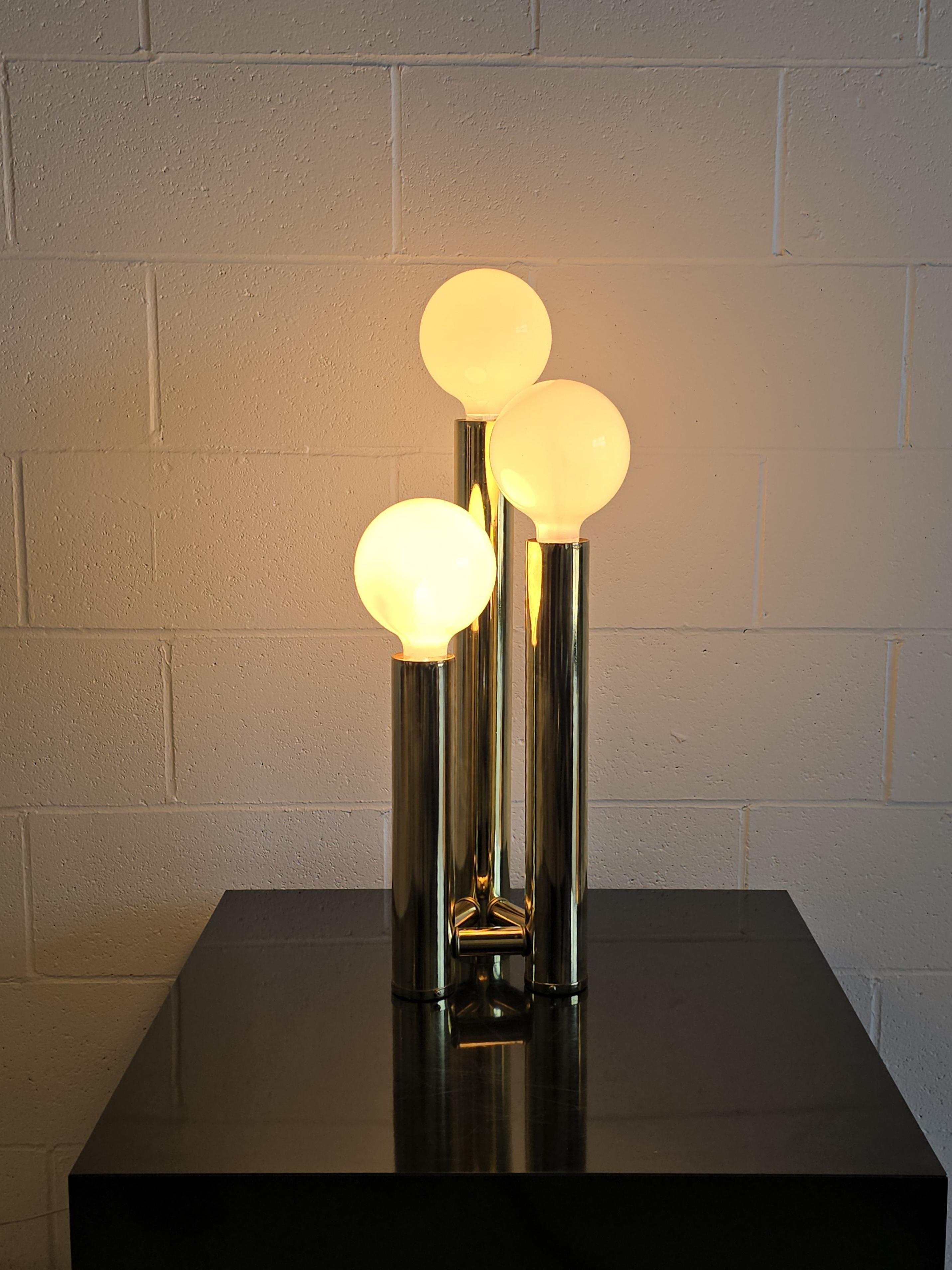 Three tier tubular brass table lamp from the 1970s. This table lamp features three tiers in varying heights. The brass base holds three G40 bulbs and has three mode switch which lights the bottom bulb, top bulbs, and all three. This brass table lamp