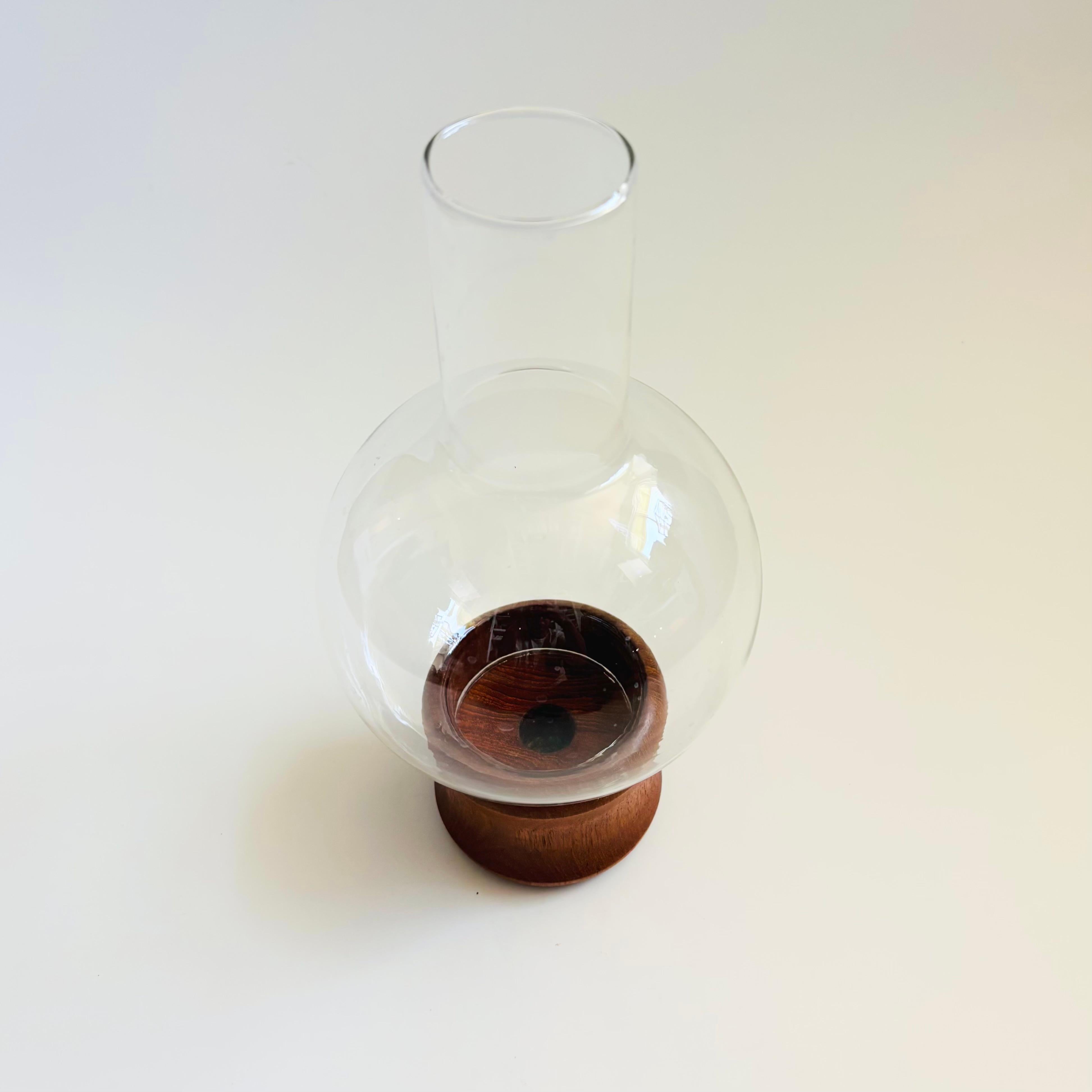 A mid century hurricane candle holder by Selandia Designs. Features a glass top that sits within a teak base. The base includes s sizes of recessed circles to hold a hurricane candle or a standard taper candle. Glass top is a simple sphere shape