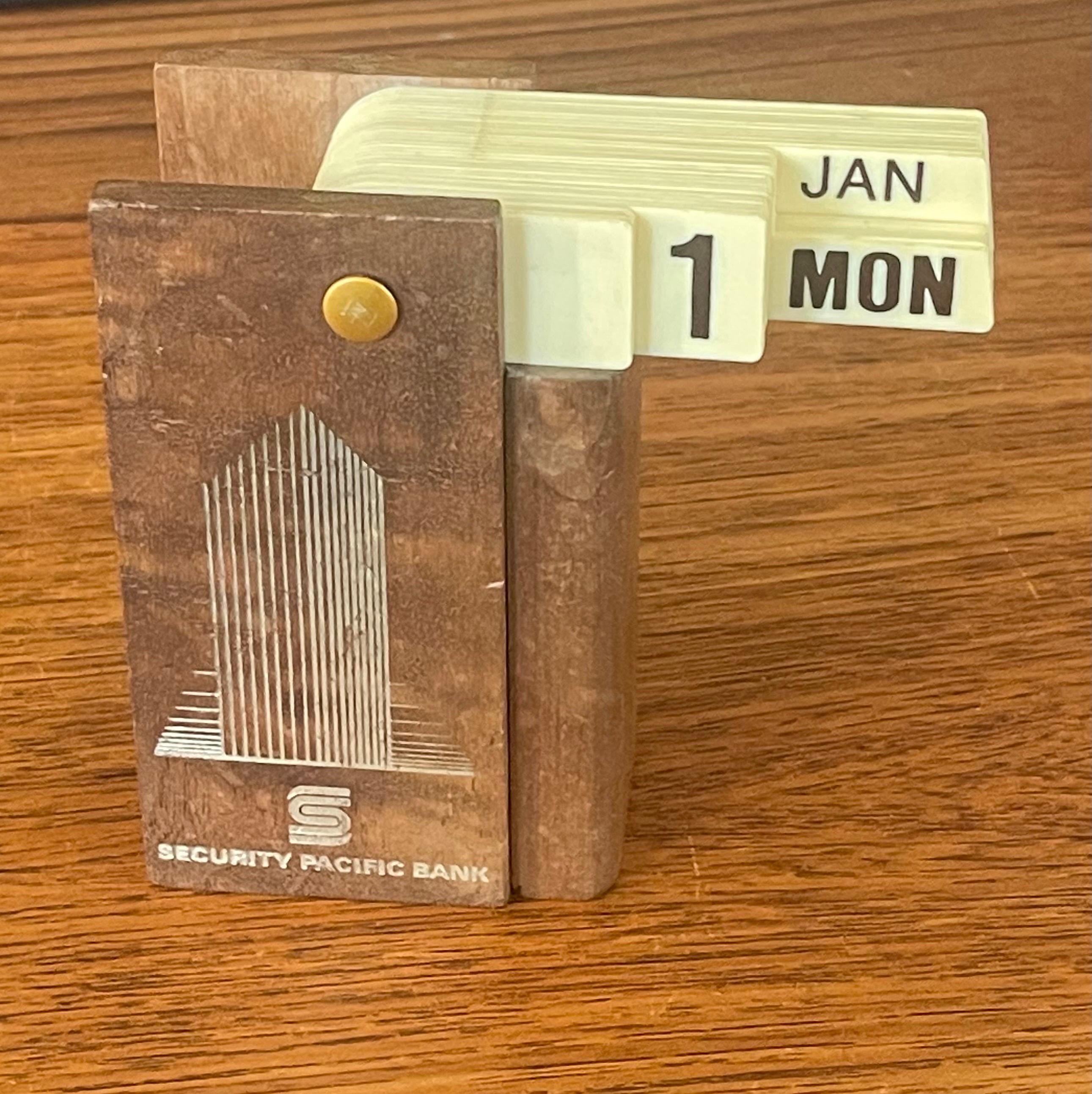 A very cool and hard to find MCM teak perpetual desk flip calendar from California's Security Pacific Bank, circa 1970's. The calendar is made of teak wood with plastic flip tabs for the month, date and day of the week. The piece is in well worn