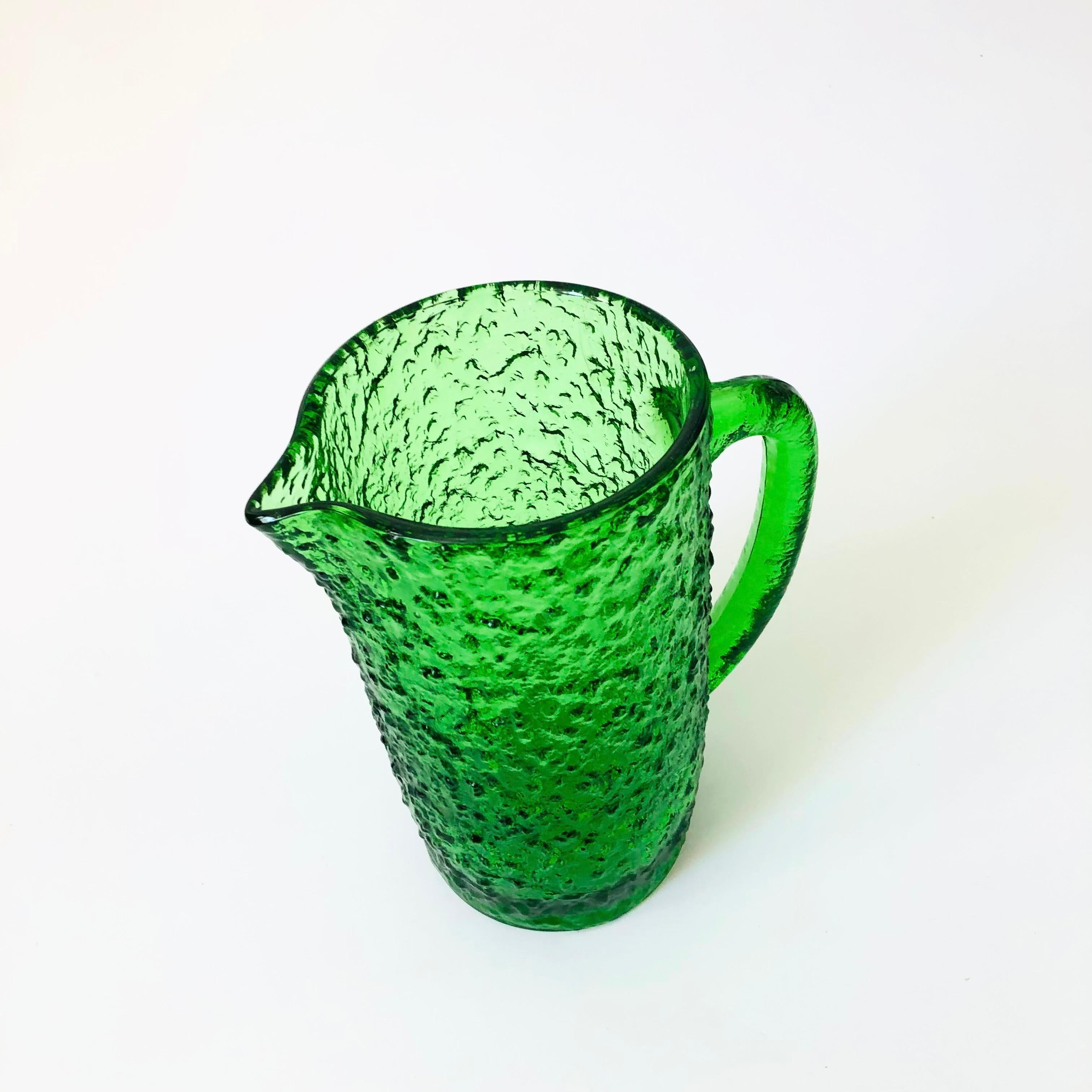 A vintage mid century pitcher made of textured glass in a vibrant green color.

