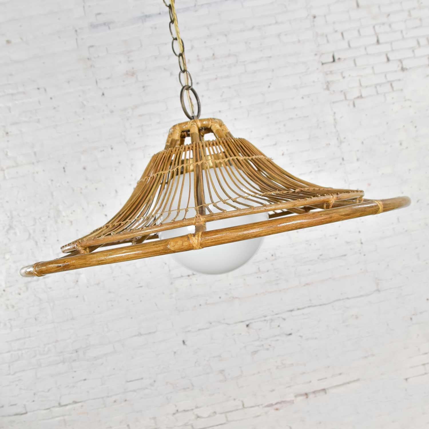 Wonderful Mid-Century Modern vintage rattan bell shaped pendant light with milk glass globe light. The ring at the top of the shade is solid brass while the canopy, fitter, and chain are brass plated. Beautiful condition with no outstanding flaws