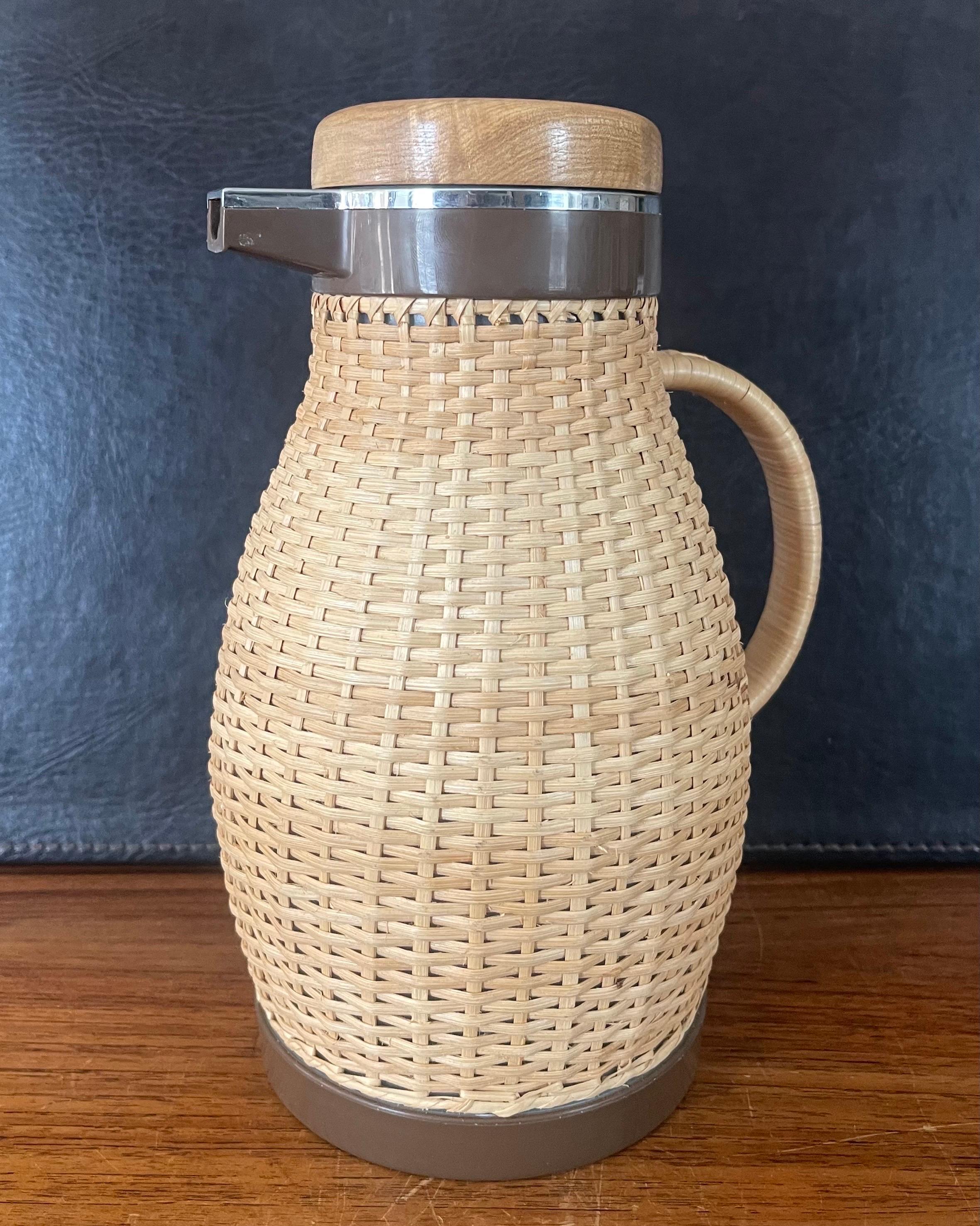 A MCM wicker wrapped thermos coffee carafe / pitcher by Corning Designs, circa 1970s. The piece is in good vintage condition and measures 8.5