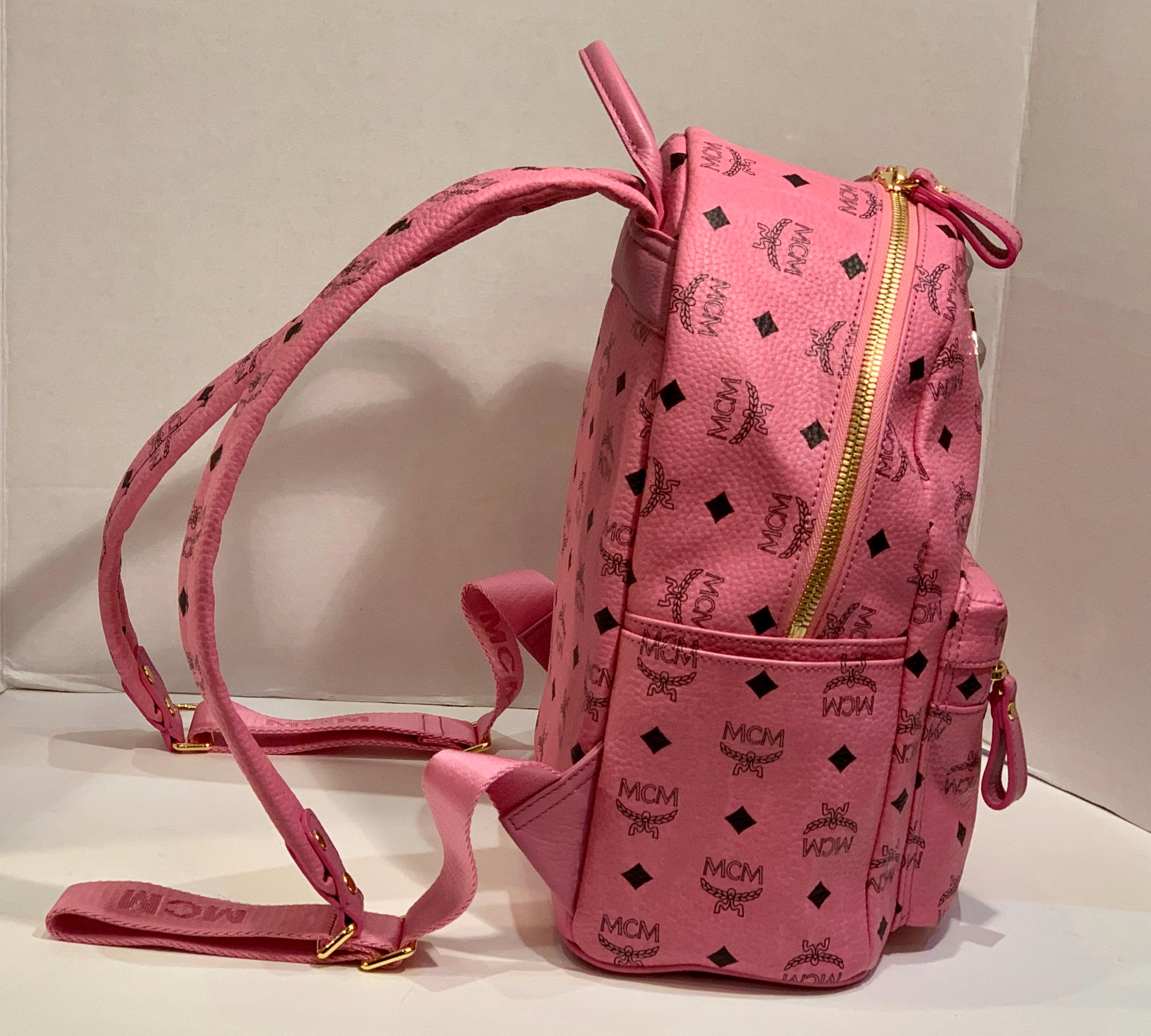 Brandneuer, mittelgroßer Rucksack der MCM Worldwide Heritage Collection aus dem charakteristischen himbeerrosa und schwarzen Visetos-Logo bedruckten Material, mit Lederbesatz und 4 Nieten auf der Front.  Der semi-belastete Look ist beabsichtigt. Die