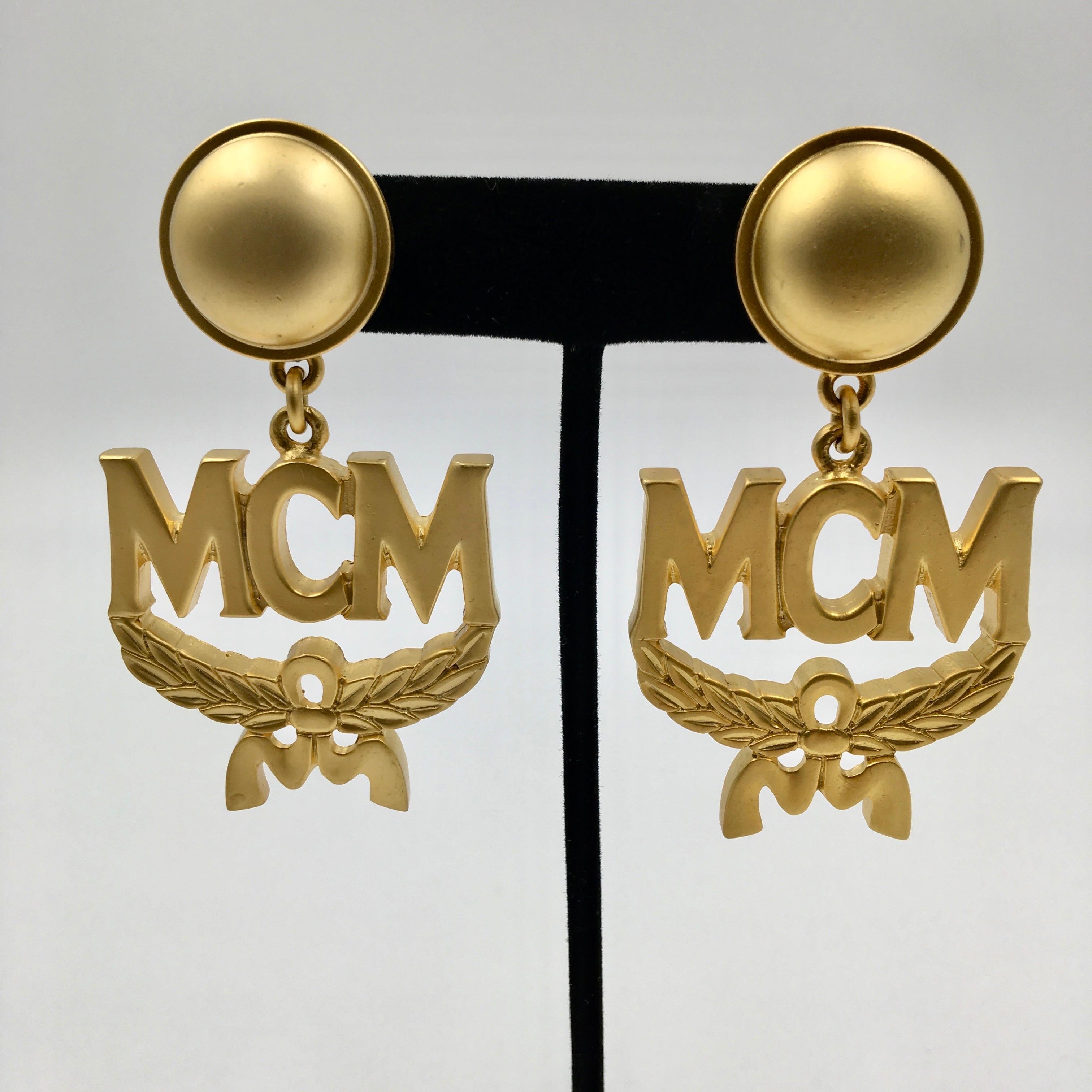 Boucles d'oreilles à clip en or mat avec logo en forme de couronne MCM. Étiquettes originales attachées. Fabriquées en Italie. 
En excellent état vintage.

Les mesures sont les suivantes :

Largeur- 1 1/2