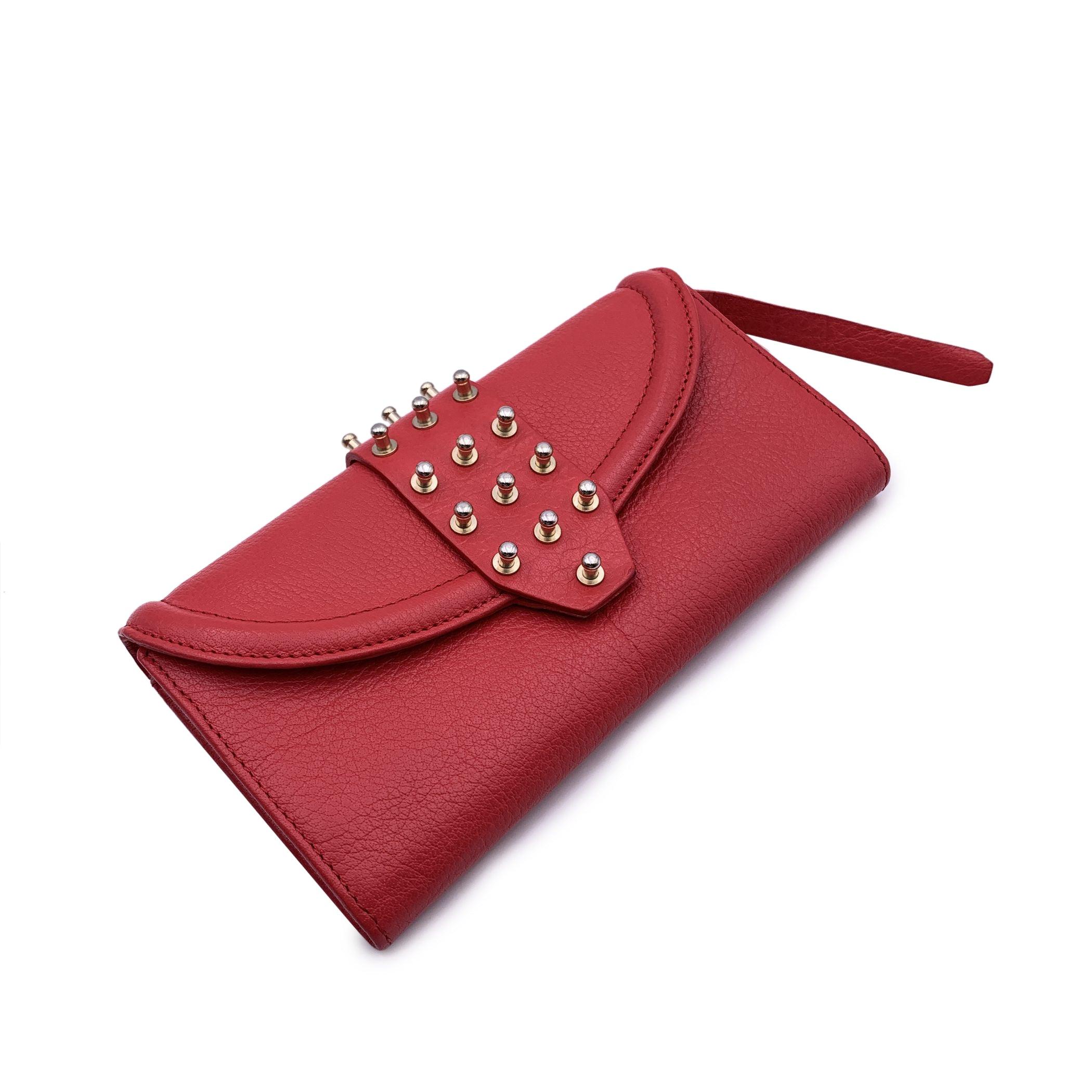 McQ Alexander McQueen Red Leather Studded Continental Wallet. Flap with button closure. Light gold studs on the flap. Fabric lining. 2 main compartments for bills inside. 1 zip compartment for coins. 2 flat open pockets, 8 credit card slots. Details