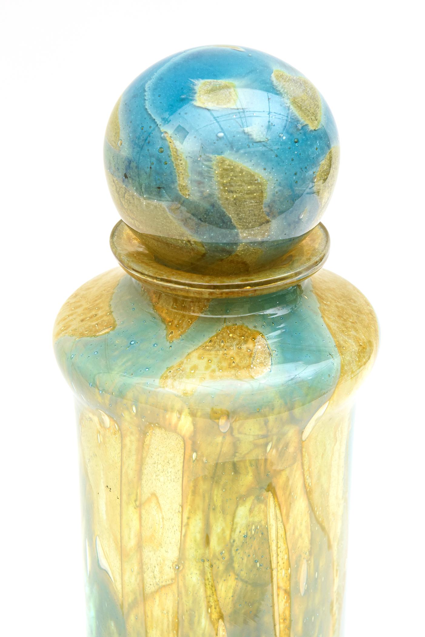 This tall commanding stellar signed vintage Mdina hand blown glass bottle/ decanter bottle / vessel / glass object is vintage from the 1970s. It has a large ball stopper and the beautiful colors range from turquoise to tiffany blue to yellows to