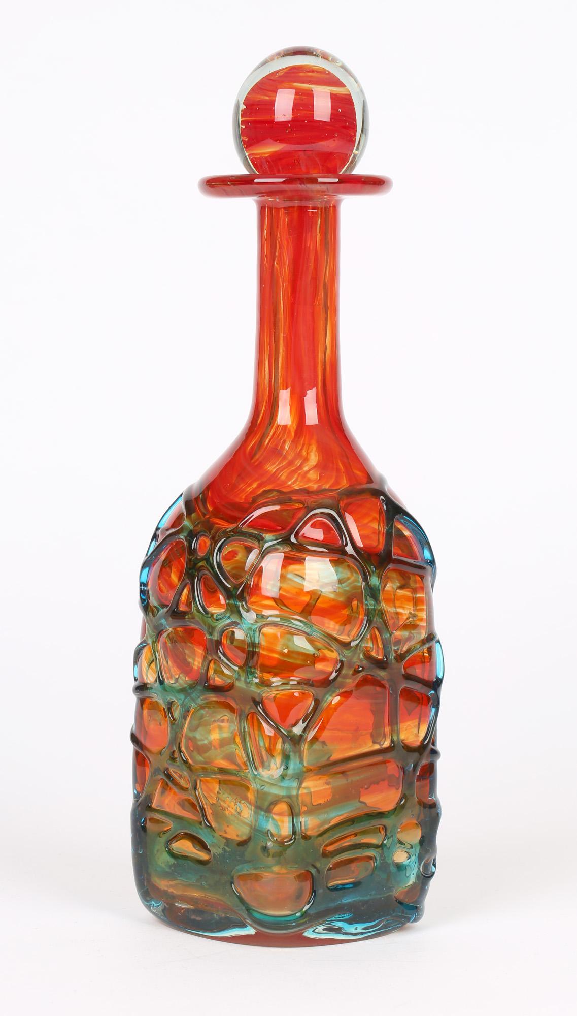 A stylish square shaped Maltese art glass decanter with stopper in a cased mottled orange color with blue glass trailing to the body. The decanter has a square shaped body standing on a flat polished base and has a narrow rounded neck with a wide