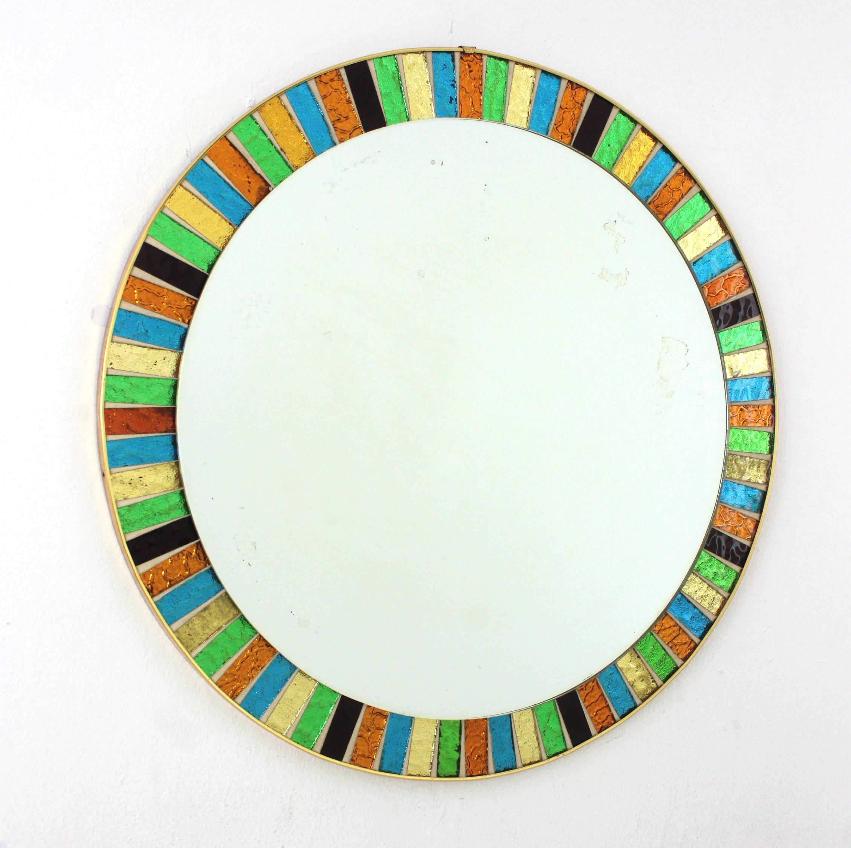 Mid-Century Modern Round Sunburst Multi-Color Mosaic Mirror, Spain, 1960s.
Eye-catching circular wall mirror featuring a frame made of pieces of textured colorful glass in yellow, green, orange, blue and garnet creating a sunburst pattern. 
Good