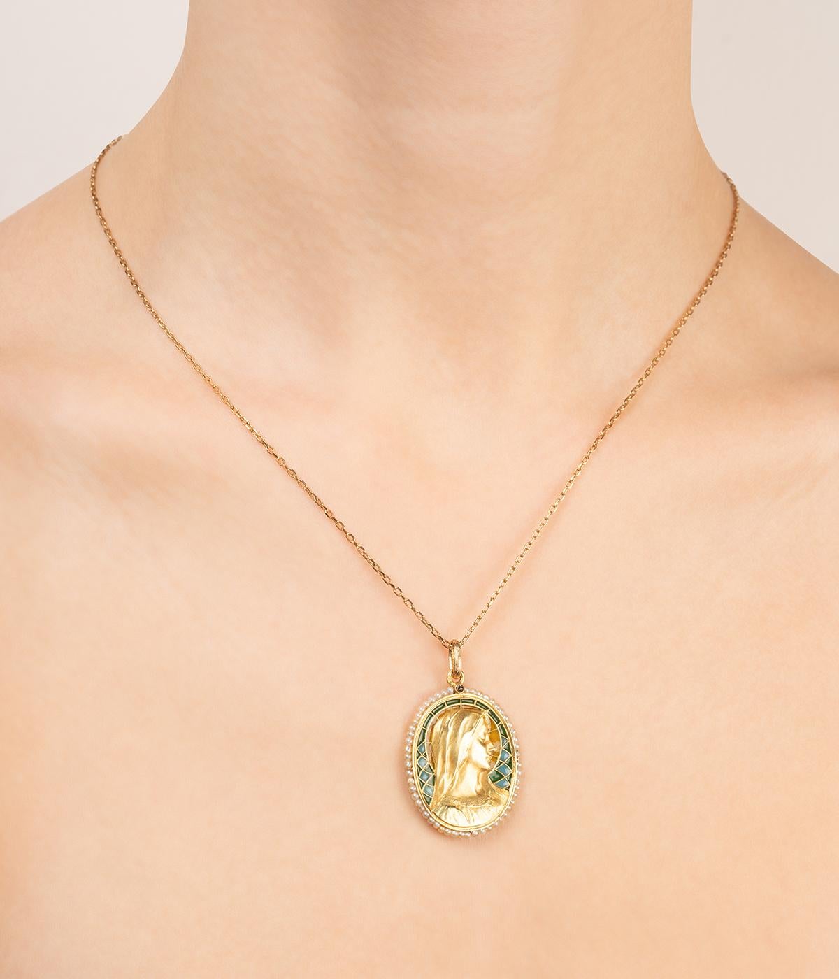 Medaglia Art nouveau in or 18 carati (750 millesimi), ornata da un profilo di vierge su un fondo di posta elettronica a giorno e circondata da una serie di perle fini. Un diamante di colore rosa si trova alla base della collana. 

Poids total du
