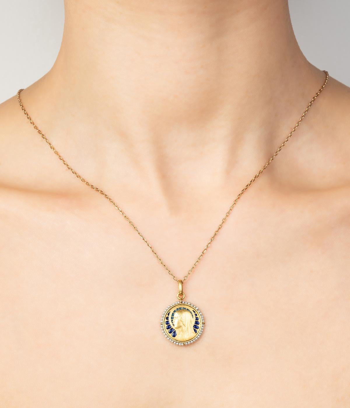 Médaille Art nouveau en or 18 carats (750 millièmes), représentant la Vierge sur un fond d'émail plique à jour dans un entourage de perles fines. 

Poids total du bijou : 2,38 g environ.
Hauteur 2,7 x Diamètre 1,9 cm.
Poinçon tête d'aigle.
Éclat à