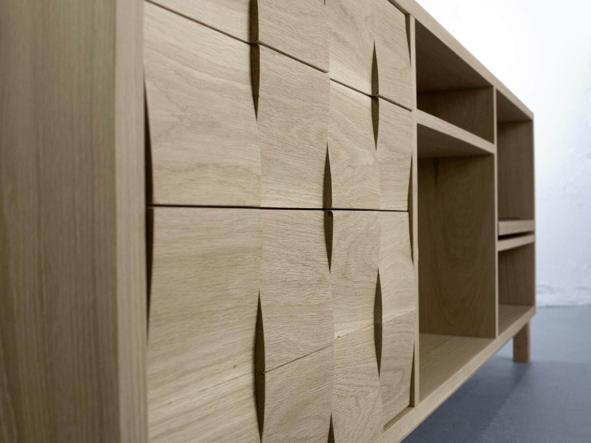 The Wave Credenza features  two drawers and a pull-down cupboard  that form a continuous wave pattern using curved oak  tiles. The drawers and media cupboard use self-opening push systems. 

At the other end a solid white oak sliding shelf opens