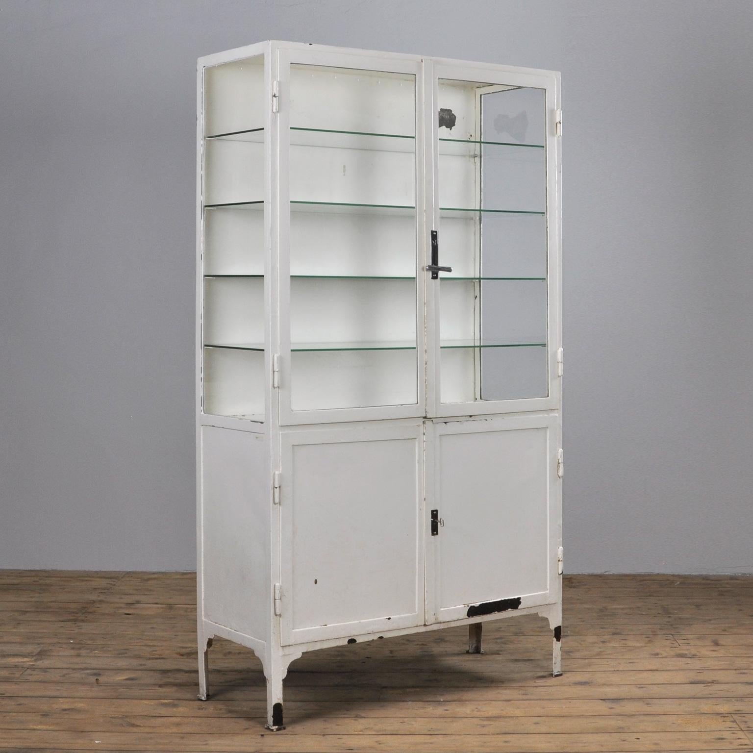 This former medical cabinet was produced in the 1940s in Hungary. It is made of thick iron and antique glass. In the upper part, there are four new glass shelves. The original locks are in perfect working condition.