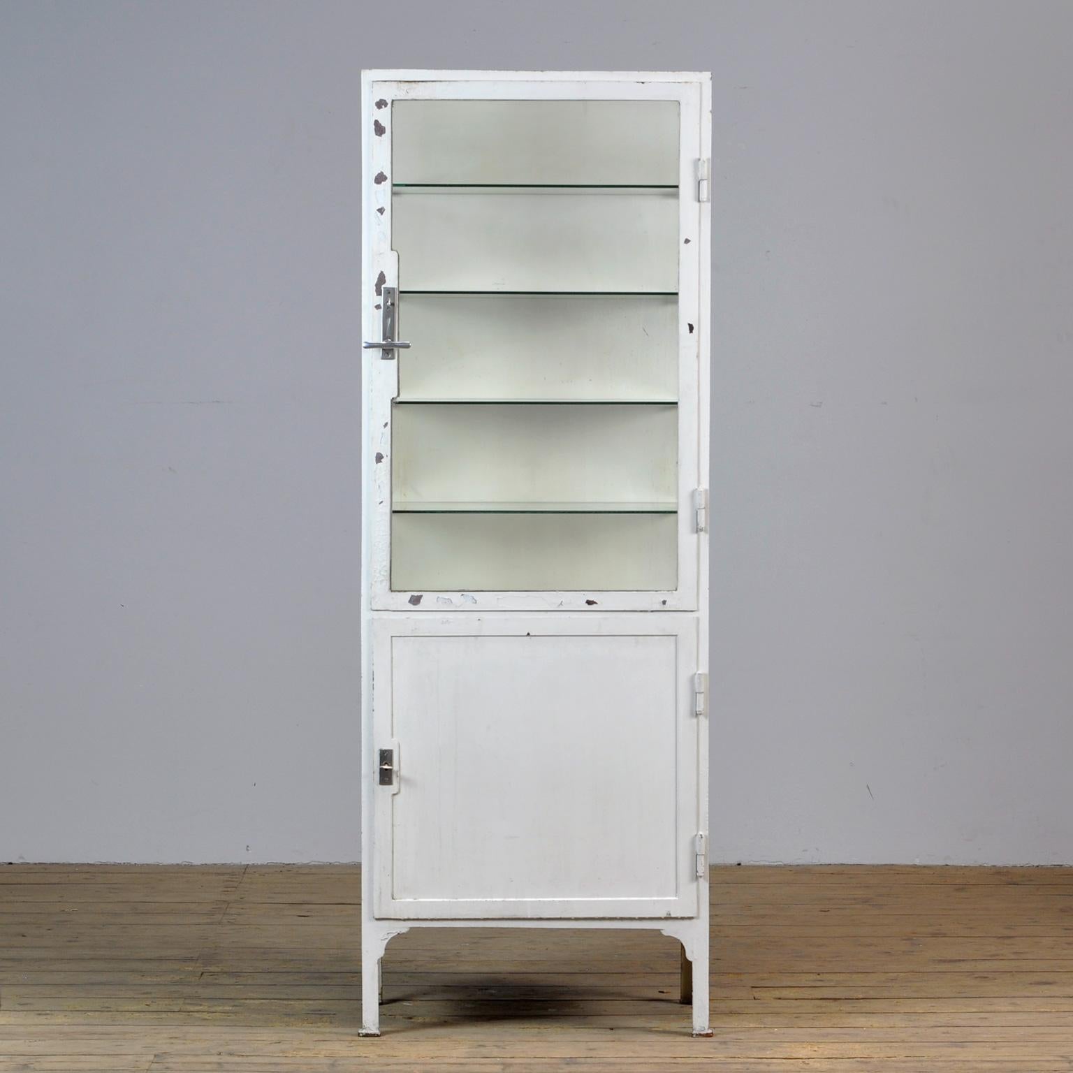 This former medicine cabinet was produced in the 1940s in Hungary and is made from thick iron and glass. With a very nice lock and handle on the top door. It features four new glass shelves.