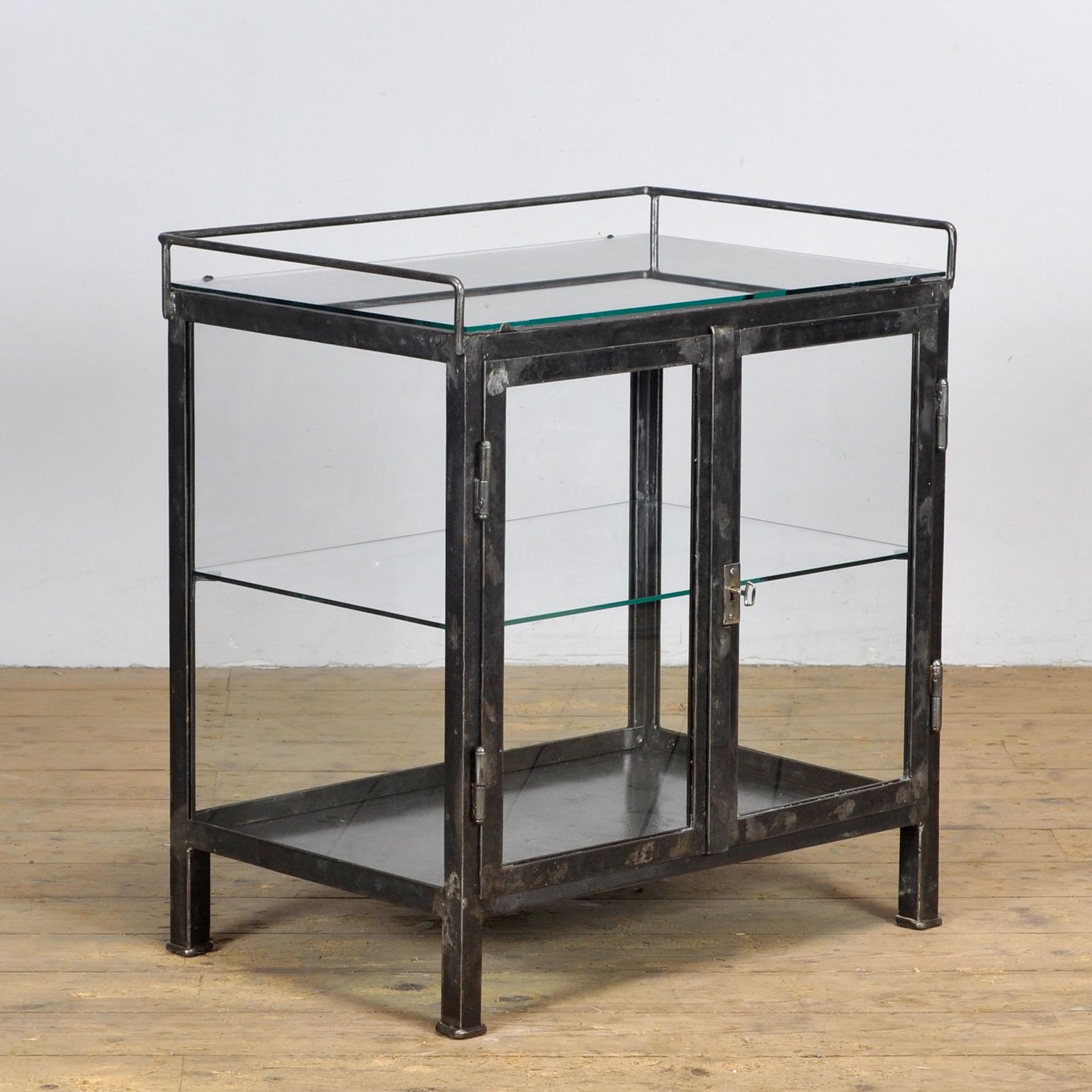 Small medical cabinet made of thick iron and glass. The cabinet has glass on 4 sides. On top a glass plate and a gllass shelf inside. The cabinet is stripped down to the metal and finished with a transparent lacquer. Good working lock / key.