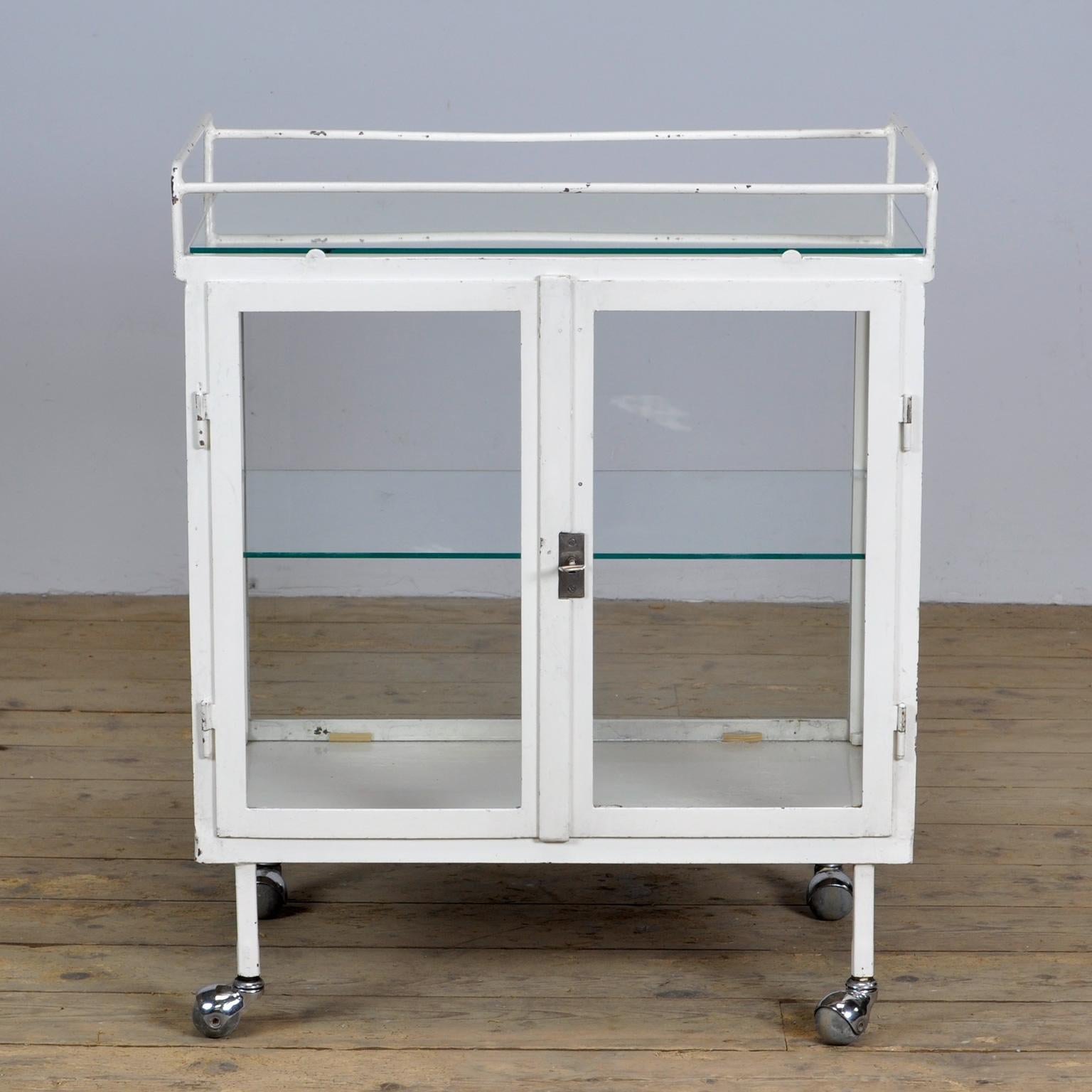 Medical trolley made of iron and glass. Produced in the 40s. The trolley has glass on 4 sides and on top a glass plate. Good working lock / key. 