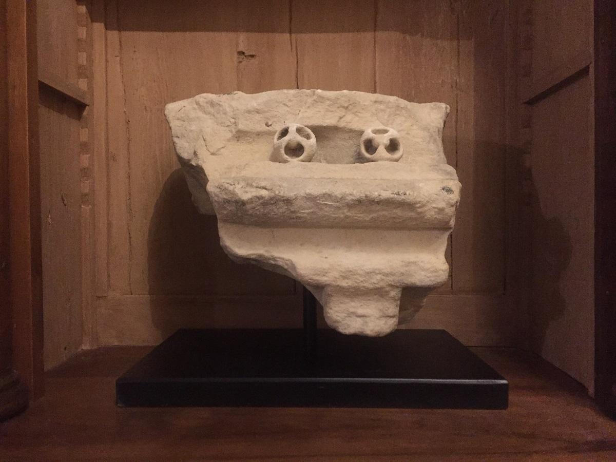 A fragment of a sandstone corbel with flat upper face, moulded transverse ledge and two protruding lobes with reserved trefoil detailing. The lower edge has fine dentiled carving and the rear face has a stepped profile.
The general form and the