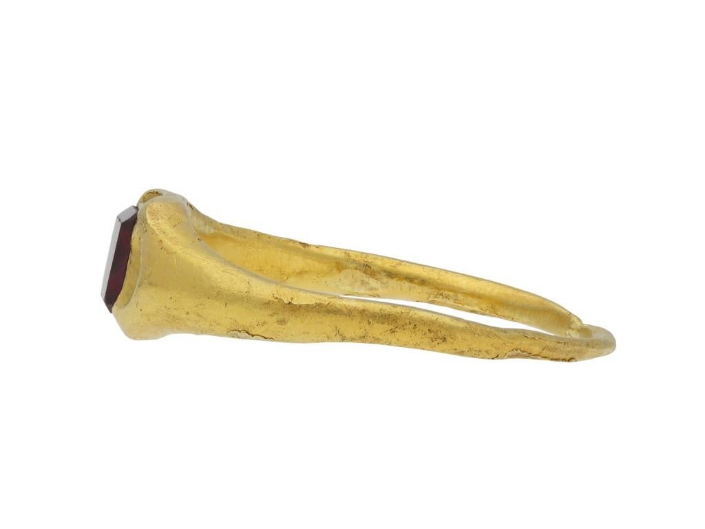 Medieval garnet gold ring. Set with a rectangular faceted garnet in a closed back rubover setting, to a scalloped quatrefoil bezel, the smoothly integrated shoulders leading through to a slim tapering solid rounded shank. Tested yellow gold,