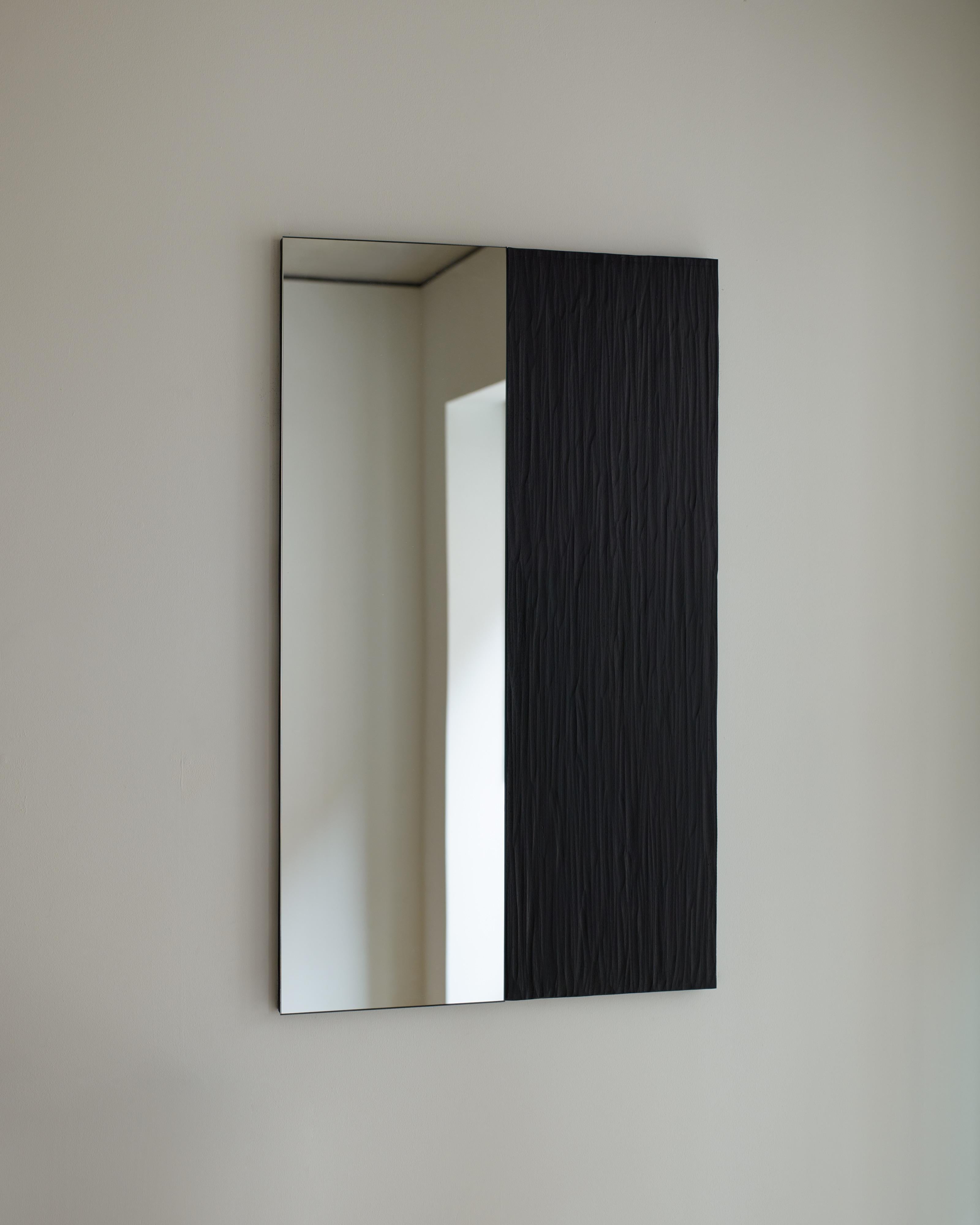 'Talisman mirror No. 4' by Rooms Studio is a single paned wall-mounted mirror with a hand-carved and blackened oak side panel. This work is part of a limited edition series entitled Talisman Mirrors, whose forms unapologetically borrow from
