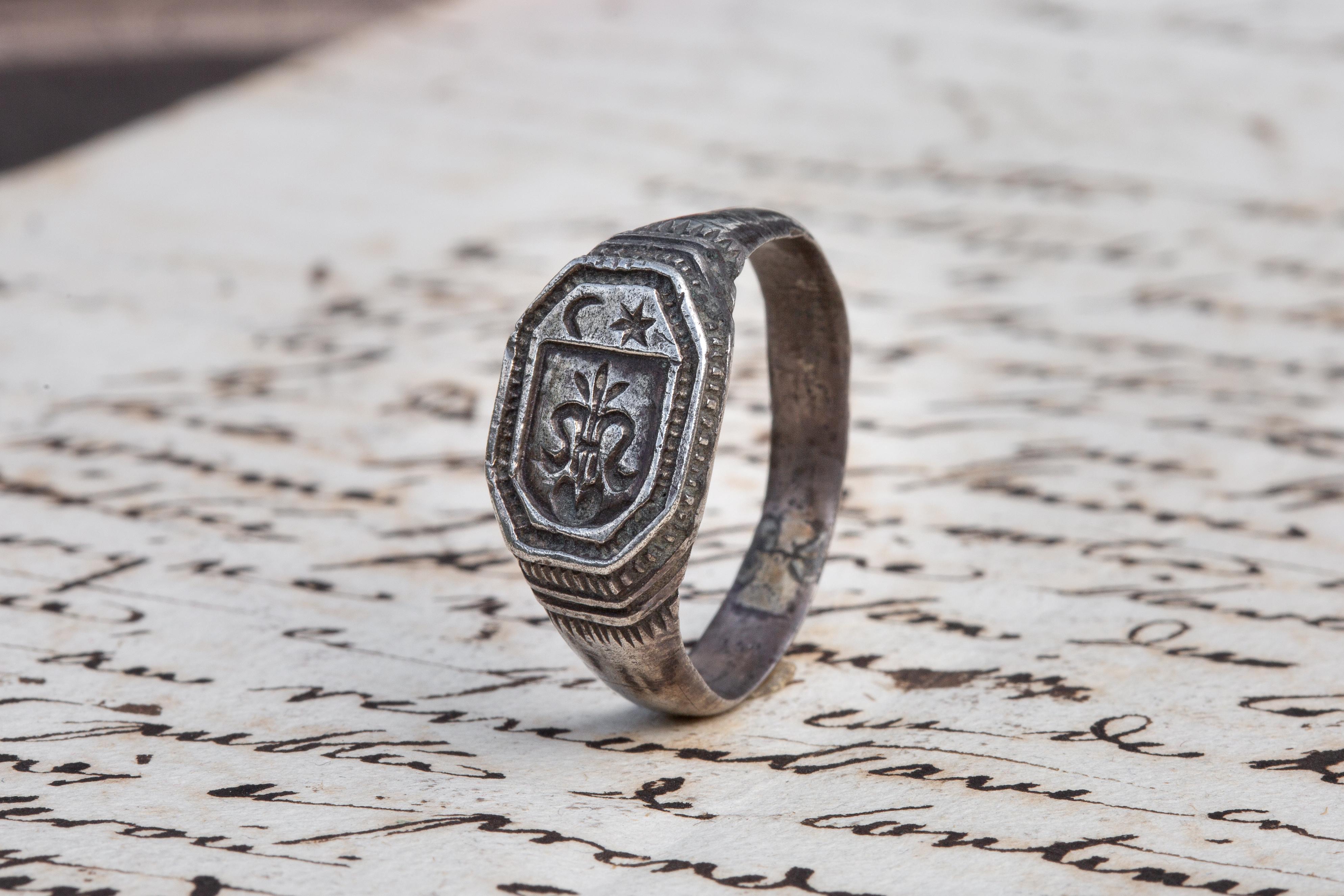 A scarce signet ring with a coat of arms intaglio crafted in silver dating to the late 14th - early 15th century. The flat, octagonal bezel is engraved with an early heraldic coat of arms consisting of a stylised fleur-de-lys with a crescent and sun