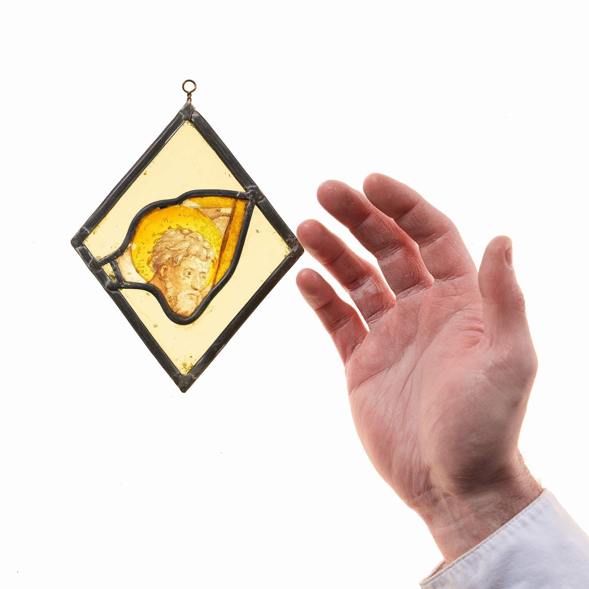 A really interesting antique stained glass window hanging panel of a saintly figure with halo dating from the medieval period, circa 1400, set within a further stained glass diamond. Likely once part of a larger window, this ecclesiastical stained