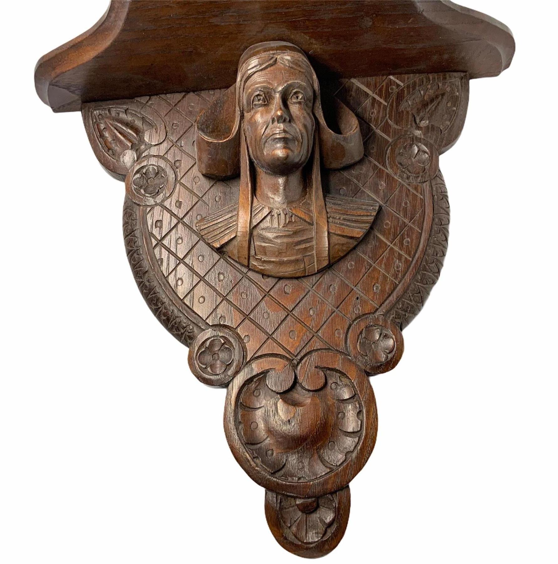 This is a wall bracket-shelf depicting a very detailed carved bust of what appear to be a scholar with medieval headwear. The wrinkles in the frontal head, the facial expressions lines and the deep gaze are noticeable. He is wearing a hat and