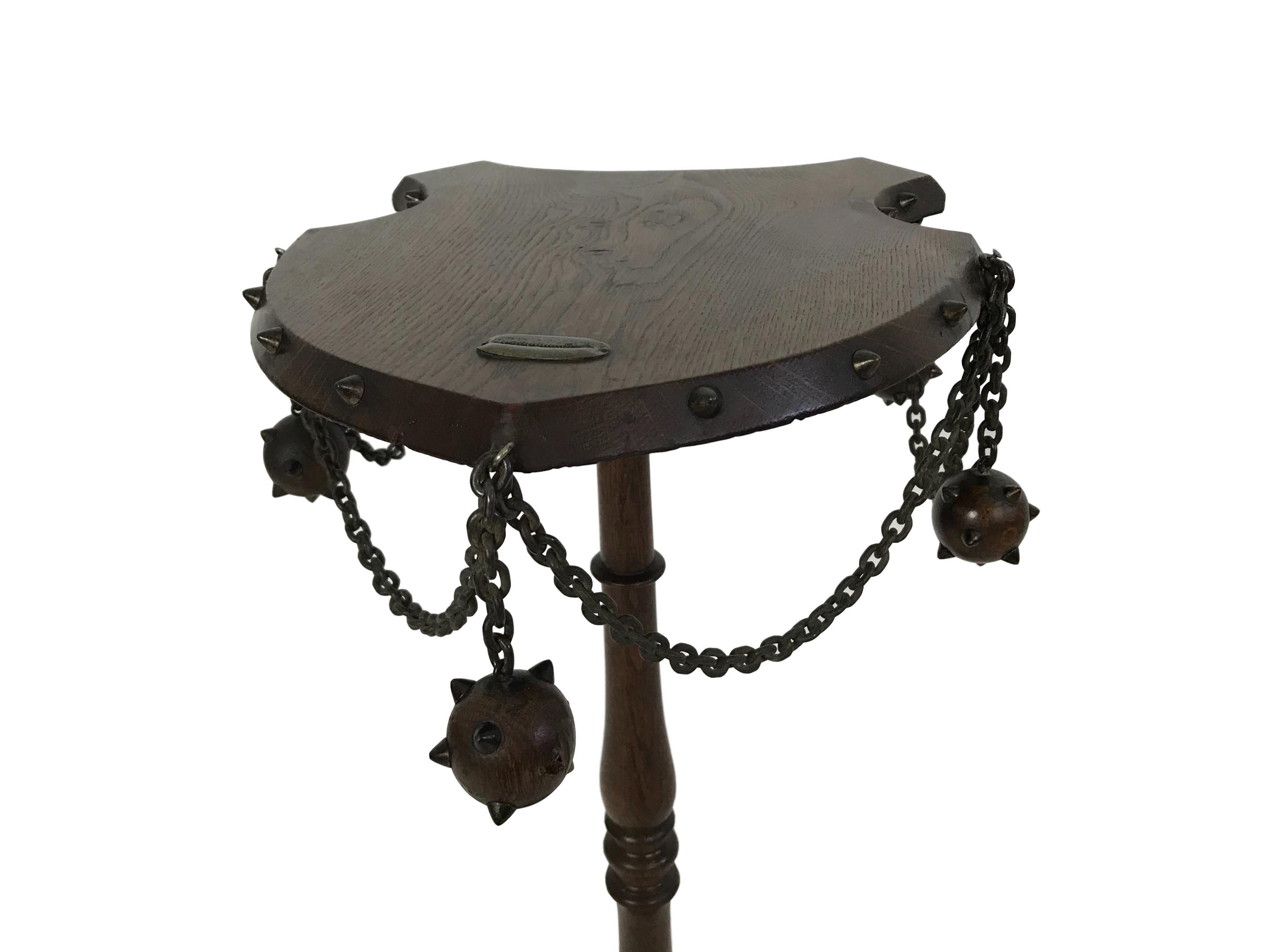 This is a one of a kind medieval themed smoking table. The top of the table is in the shape of a shield with a zinc match strike fixed to it. Along the sides hang wood mace balls with metal spikes and chain. Metal spikes adorn the edges of the