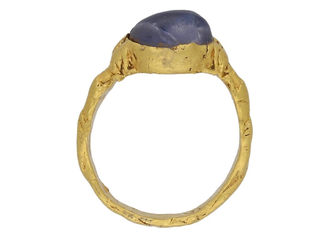 Medieval zoomorphic sapphire ring. An important piece, horizontally set with a sapphire cabochon, originally used as a bead with lengthwise drill hole, in a closed back collet setting, bezel gripped either side by two pairs of gaping mouths of