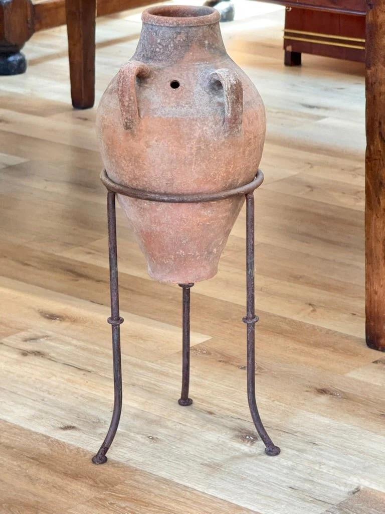 Jarre à olives en terre cuite cultivée à la main, avec des anses en boucle et une patine d'usage, probablement au 19e siècle en Méditerranée. Surélevée sur un socle en fer personnalisé, elle constitue un accent sculptural au caractère rustique