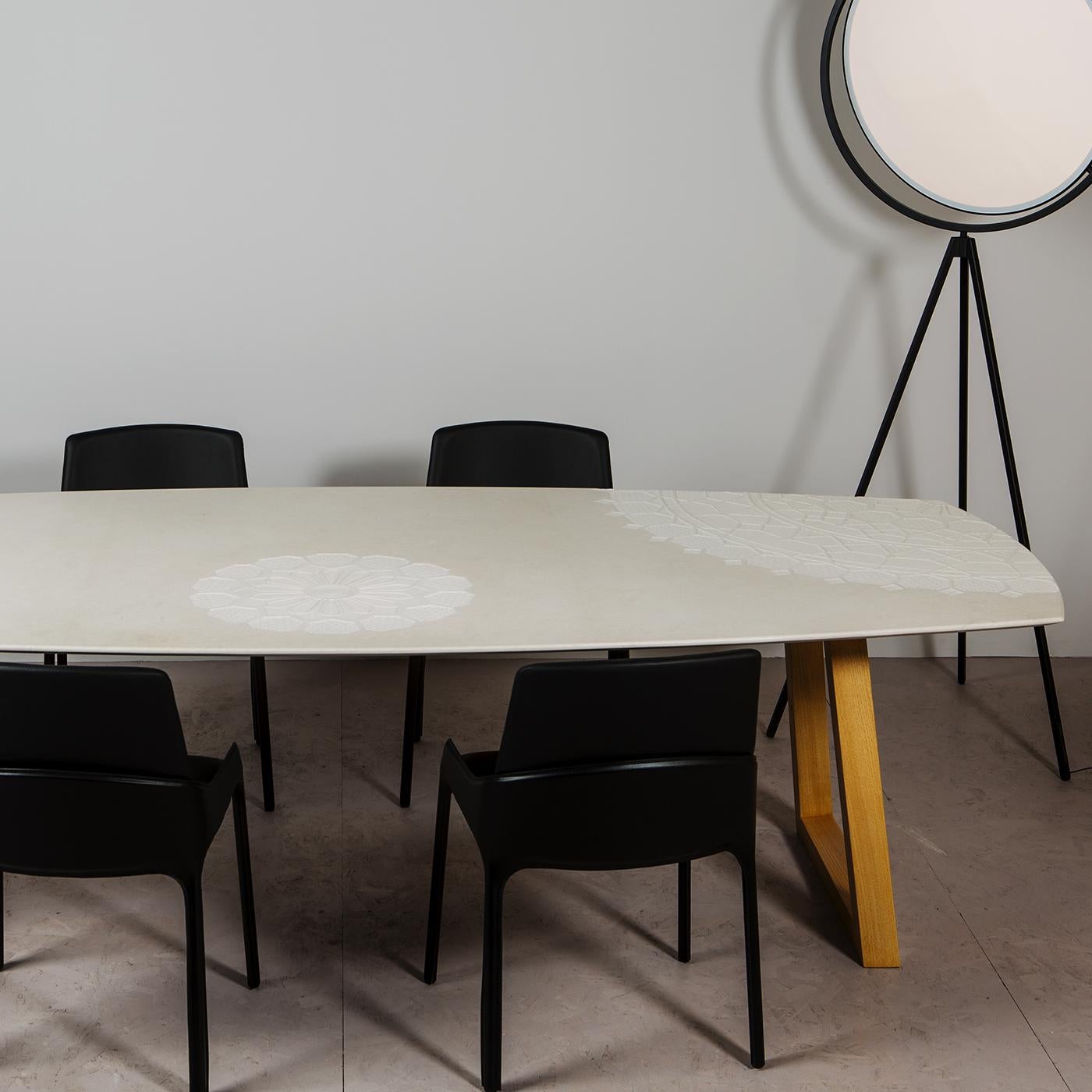This modern and striking dining table is made of Crema Tunisi stone. The top displays an exquisitely sculpted surface, showcasing superb doilies and coverings. The linear and elegant base structure is made of natural-finished wood. This