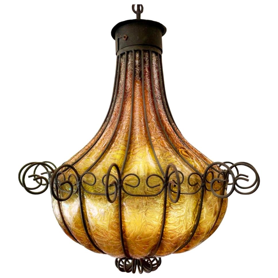 Mediterranean wrought iron caged blown amber glass chandelier, murano art glass. Exceptional caged glass chandelier. Gorgeous wrought iron work. Rare Empire “inverted bell’ form. 1 bulb.
Chain is approximately 11’ long and cord extends an