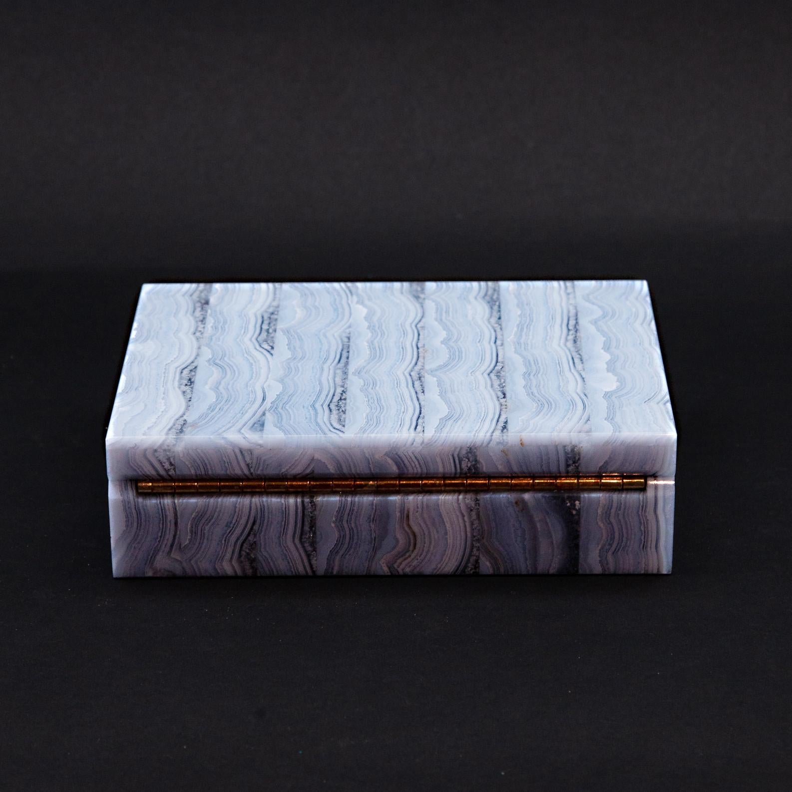 Blue lace agate box with light blue and white and translucent stripes. Fine black felt interior and gold tone hardware. Said to be a relaxing stone because of cool hues. Some healers say that the blue lace agate improves communication.

Measures: