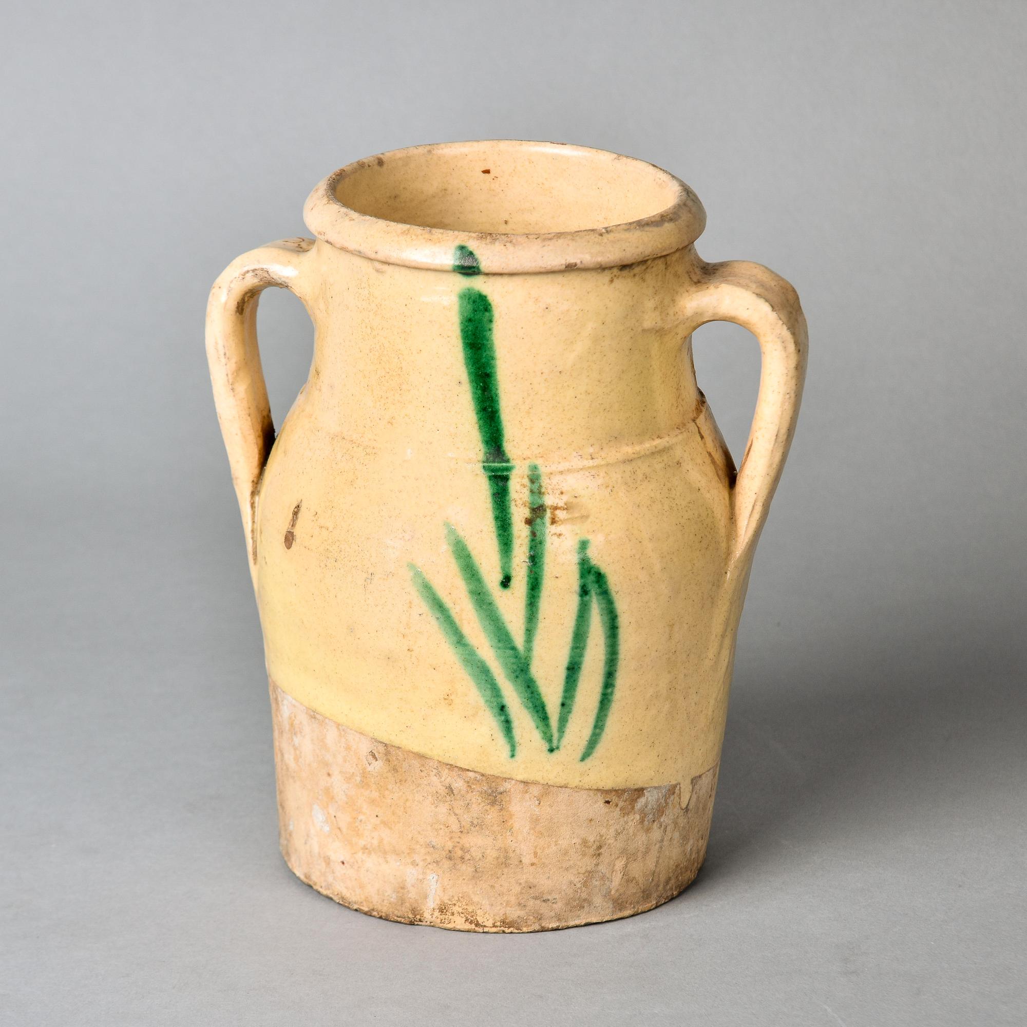 Realizzato in Francia, questo vaso tradizionale francese rustico del 1900 circa ha due manici curvi e uno smalto color senape chiaro con un disegno di rami verdi. Alcuni segni di usura sparsi con scaglie sullo smalto, ma nessuna riparazione o