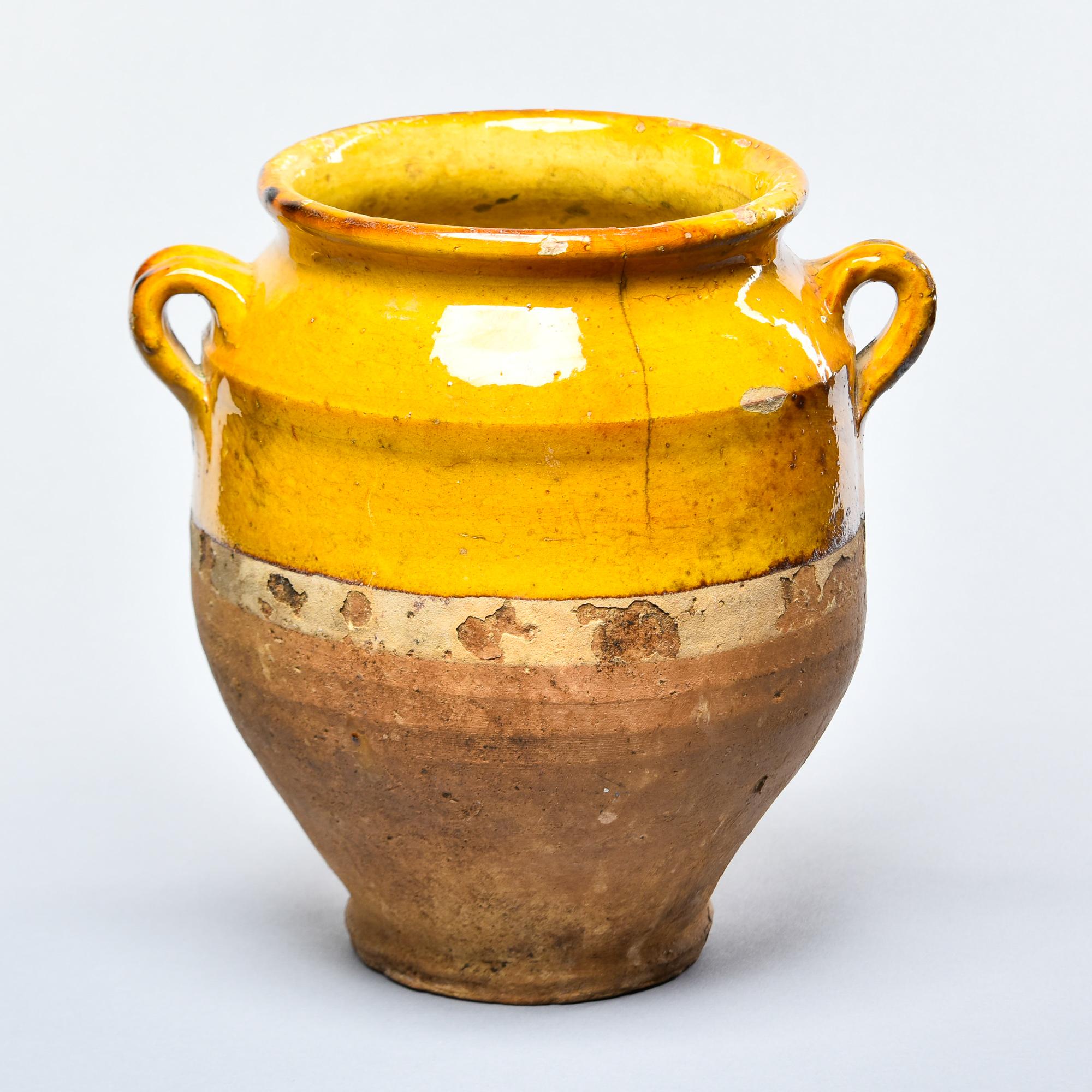 Found in France, this French confit jar dates from approximately 1915. This piece stands 9.5” high and has the traditional form with a wide vessel body and two handles on the sides with a mustard-colored glaze on the outside top half and fully