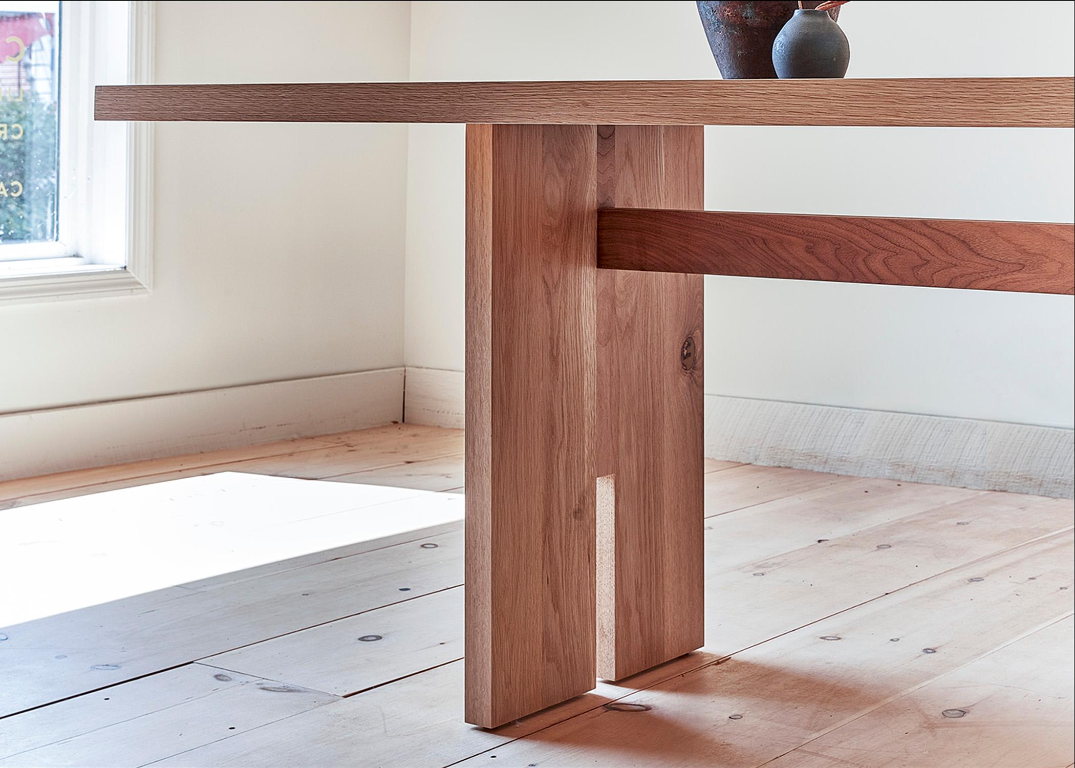 This custom dining table is hand-made in the United States with all hardwood construction. It features a modern table design with a solid white oak body and a minimalist walnut inlay detail and stretcher. Naturally occurring knots are celebrated,