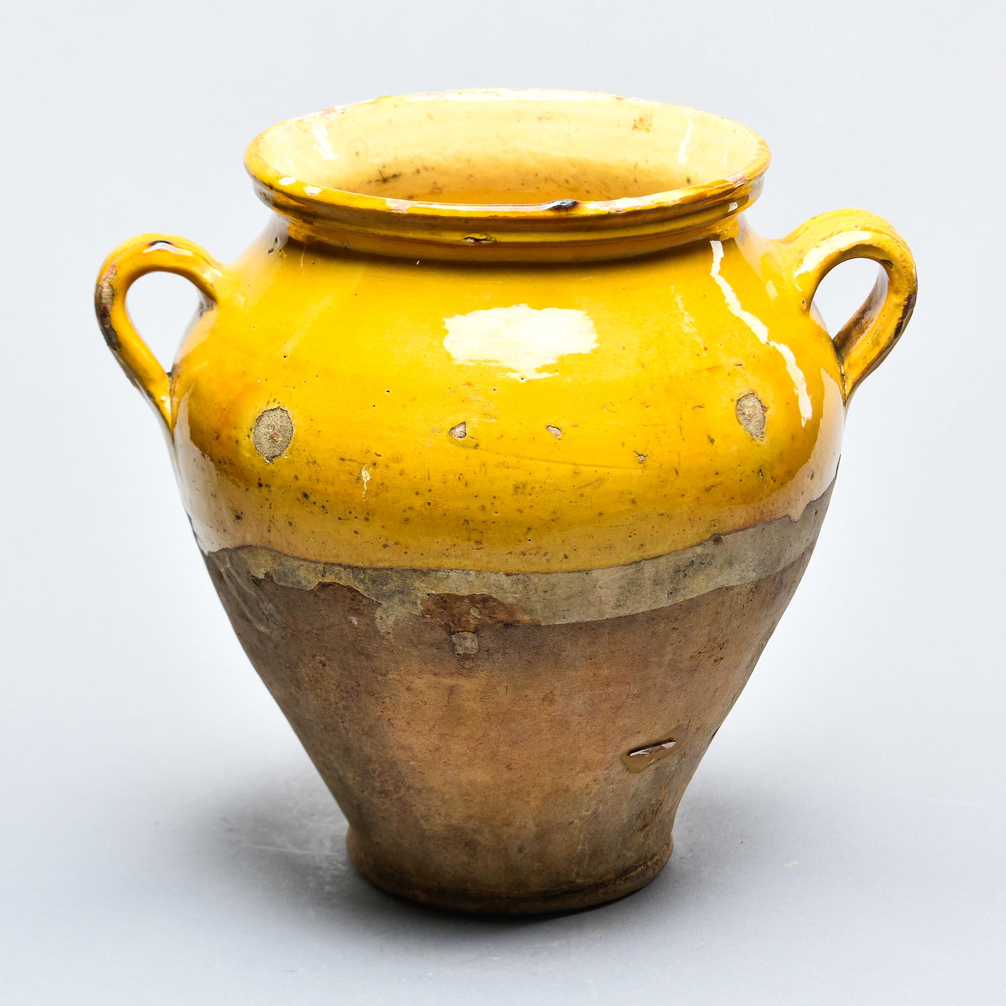 Found in France, this French confit jar dates from approximately 1910. This piece stands 10” high and has the traditional form with a wide vessel body and two handles on the sides with a mustard-colored glaze on the outside top half and fully glazed