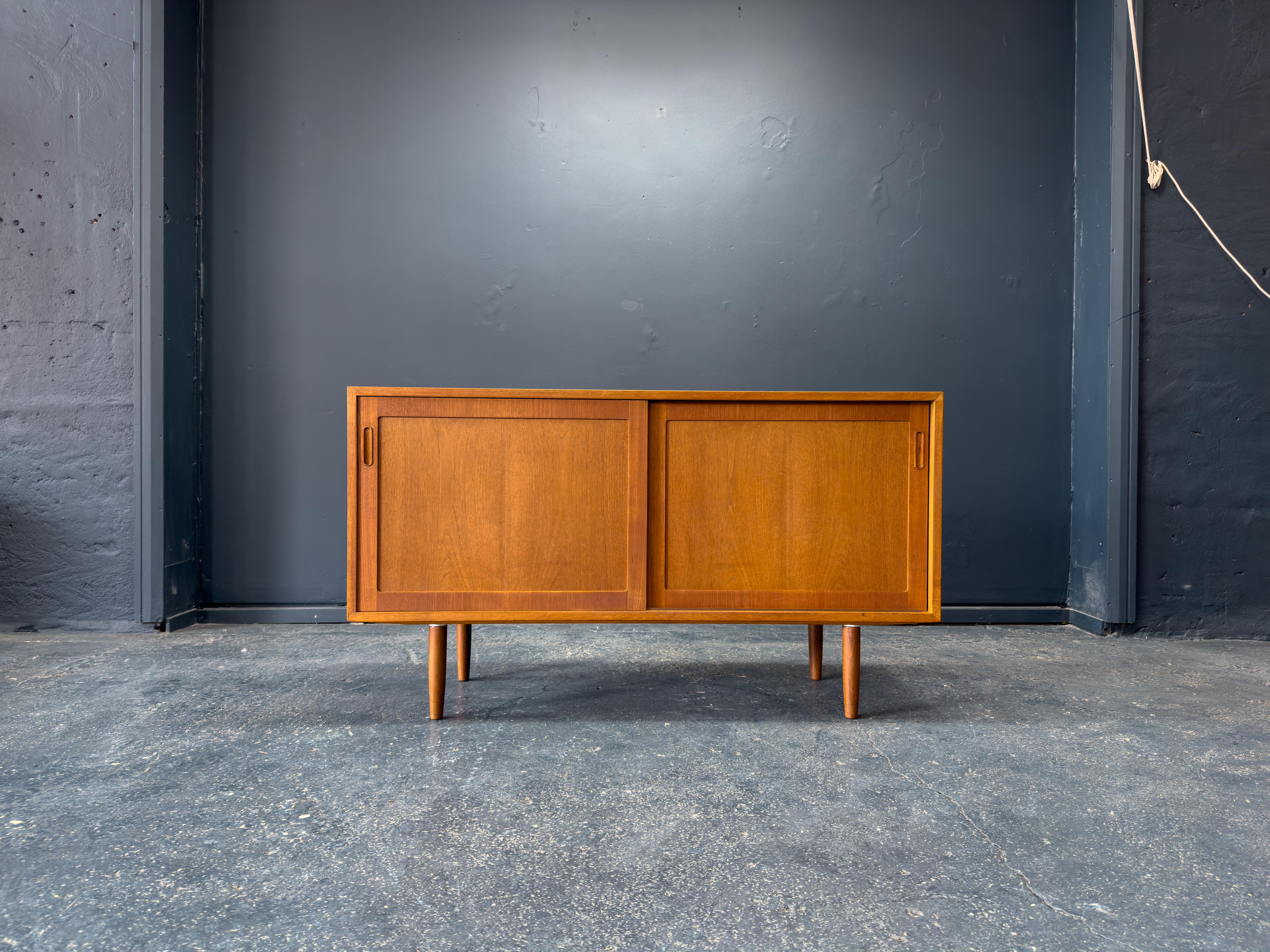 Questa credenza compatta in teak è una masterclass del design minimalista danese, che combina linee pulite, falegnameria precisa e un'estetica calda ed equilibrata. Poggiato su gambe sottili e affusolate, il pezzo ha una posizione raffinata che