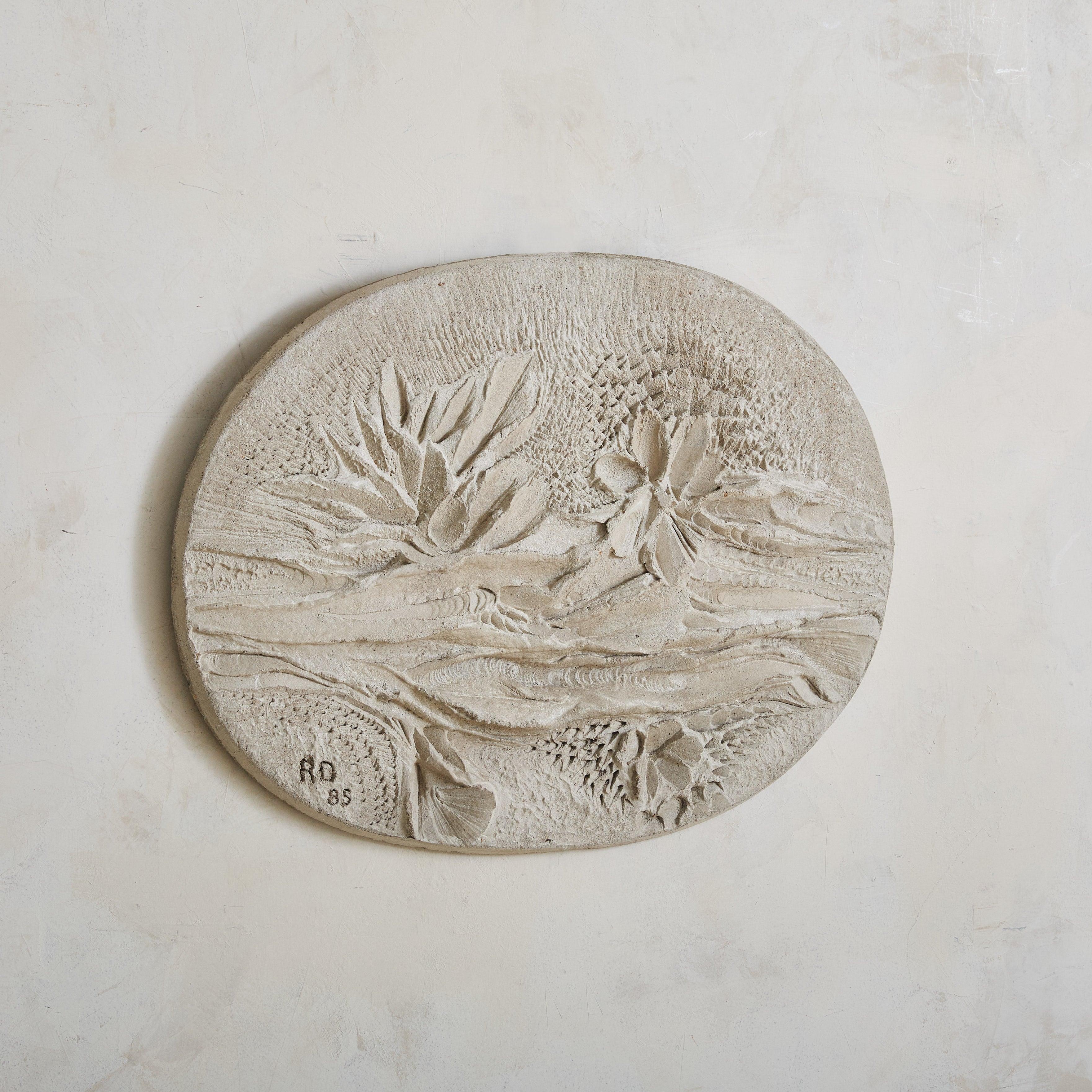 A medium oval wall sculpture by French artist Roger Desserprit. This bas-relief, crafted of concrete, has a surface finished in white cement plaster. Abstract floral motifs and intricate texture make it interesting from every angle. Signed and dated