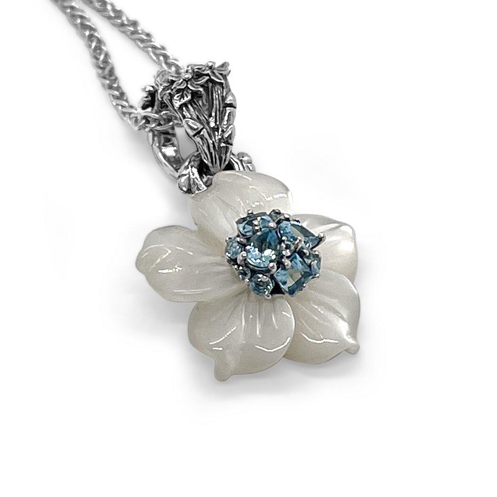 Lassen Sie sich von der zarten Schönheit des Blütenanhängers Medium White Mother-of-Pearl mit Schweizer Blautopas verzaubern, einem charmanten Meisterwerk, das mühelos Eleganz mit Weiblichkeit verbindet. Dieser mit akribischer Präzision gefertigte