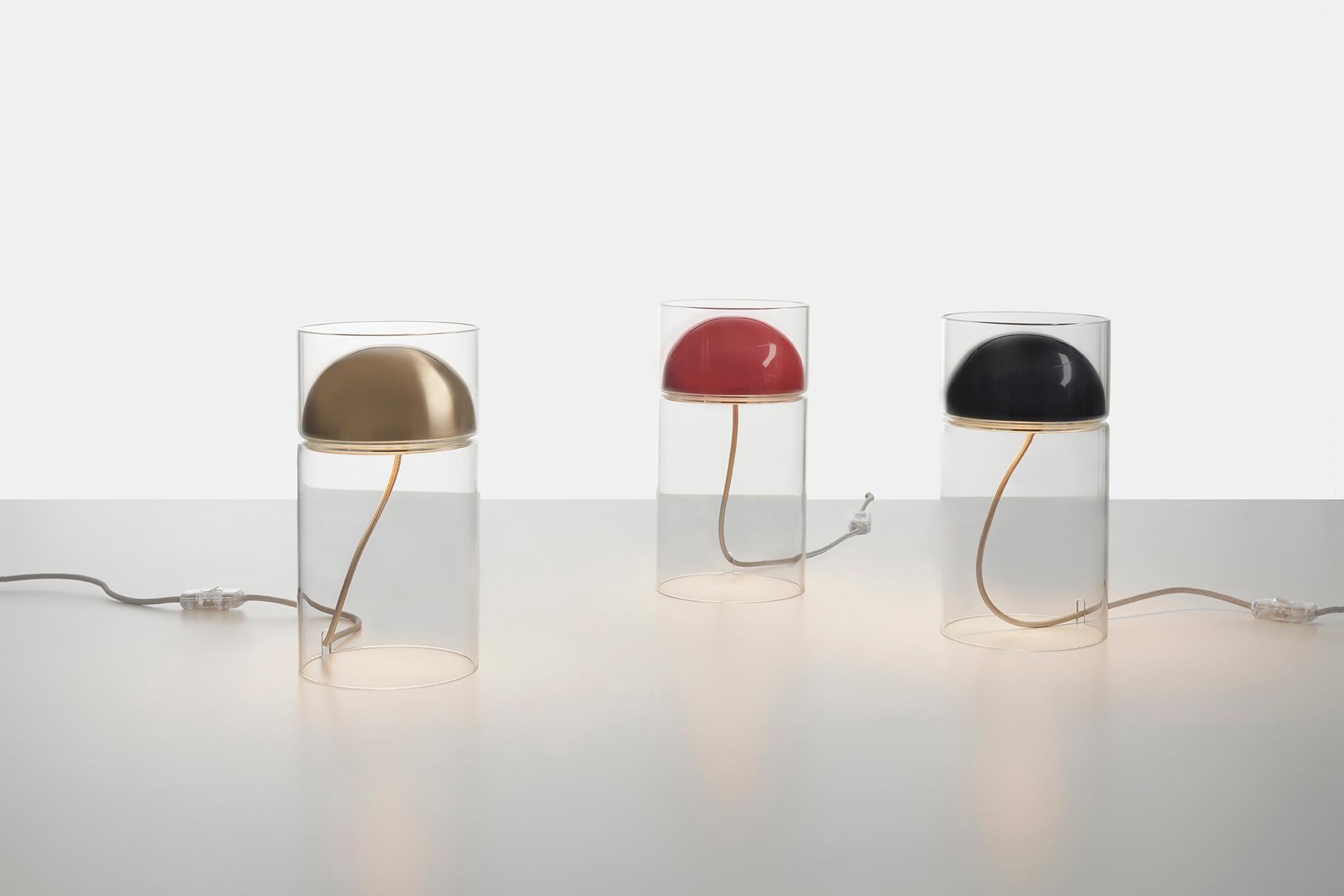 Un minimalisme formel pour une lumière douce et chaleureuse. Medusa est une lampe de table en verre basée sur le principe élémentaire de l'incorporation d'un dôme métallique dans un cylindre : le dôme contient la source lumineuse et le cylindre de