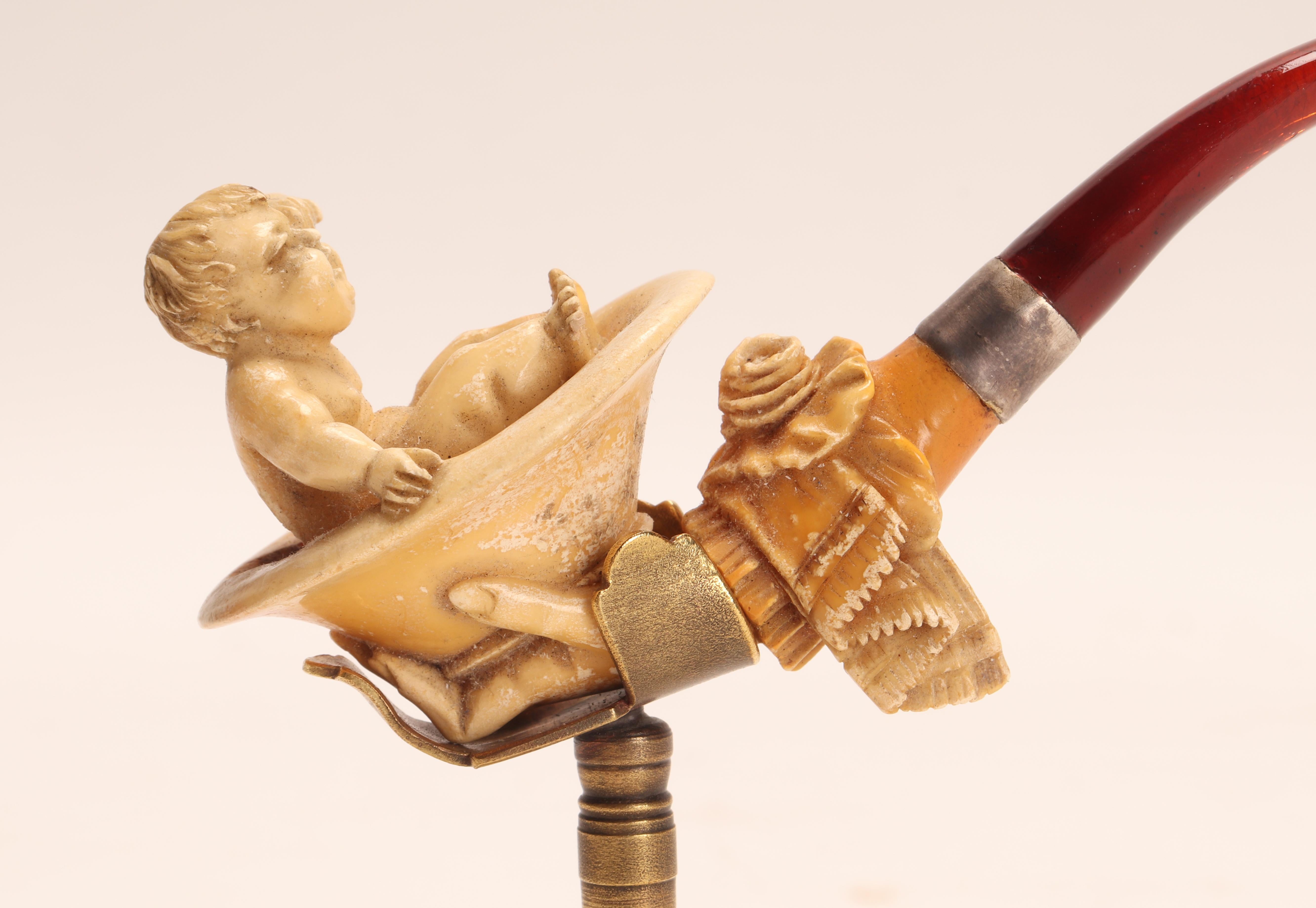 Tobacco taster pipe, made out of carved meershaum, with silver and amber mouthpiece with a silver band. One hand holds a tub where a child is sitting. Original case. Vienna, Austria circa 1880. (The stand is for photographic use only, not for sale).