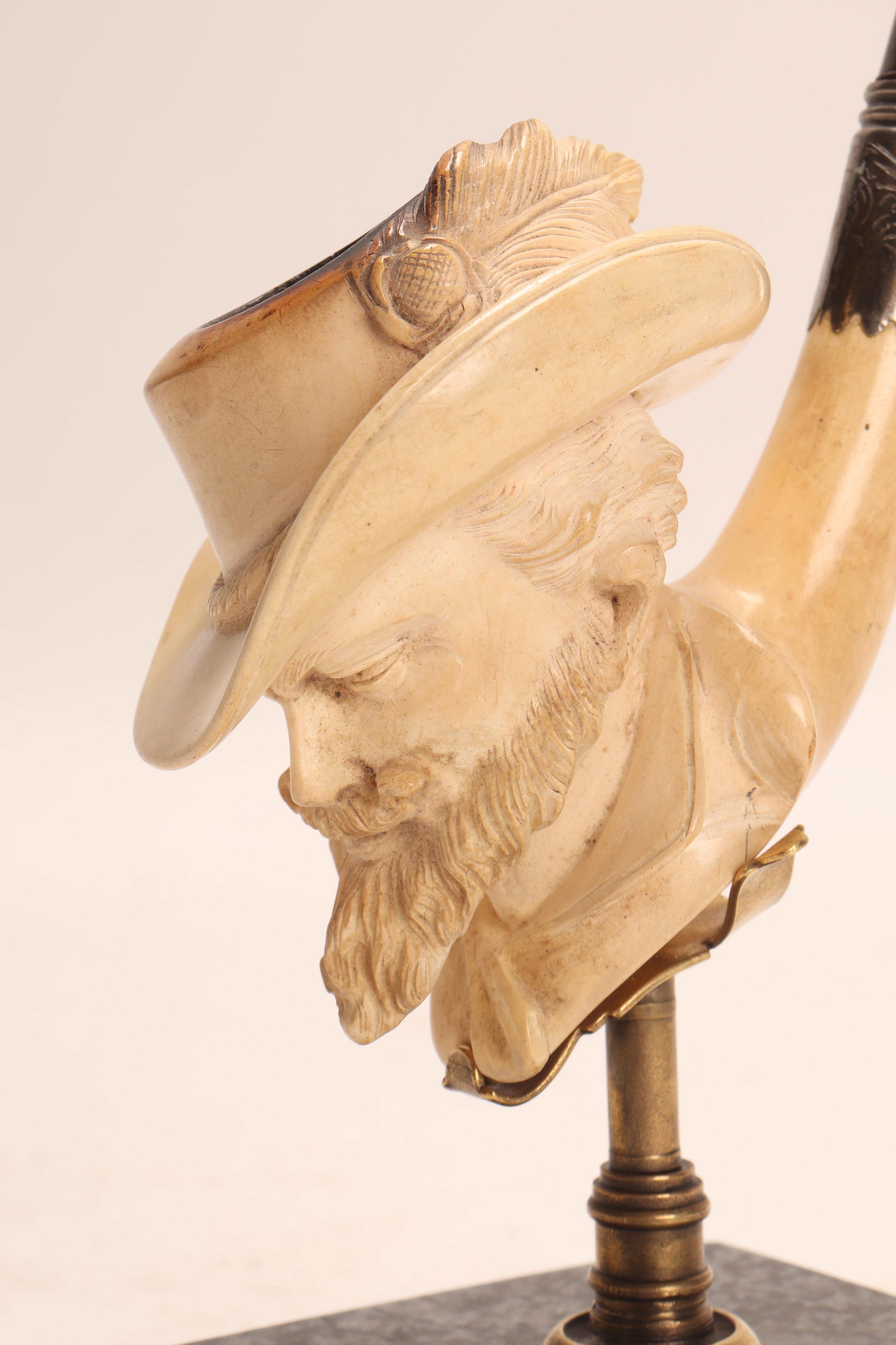 Carved meershaum pipe, with amber mouthpiece and silver band. In the bowl of the pipe, the head of General Custer is depicted, with a beard and mustache, wearing a hat with a feather. Original case. Vienna, Austria circa 1880. (The stand is for