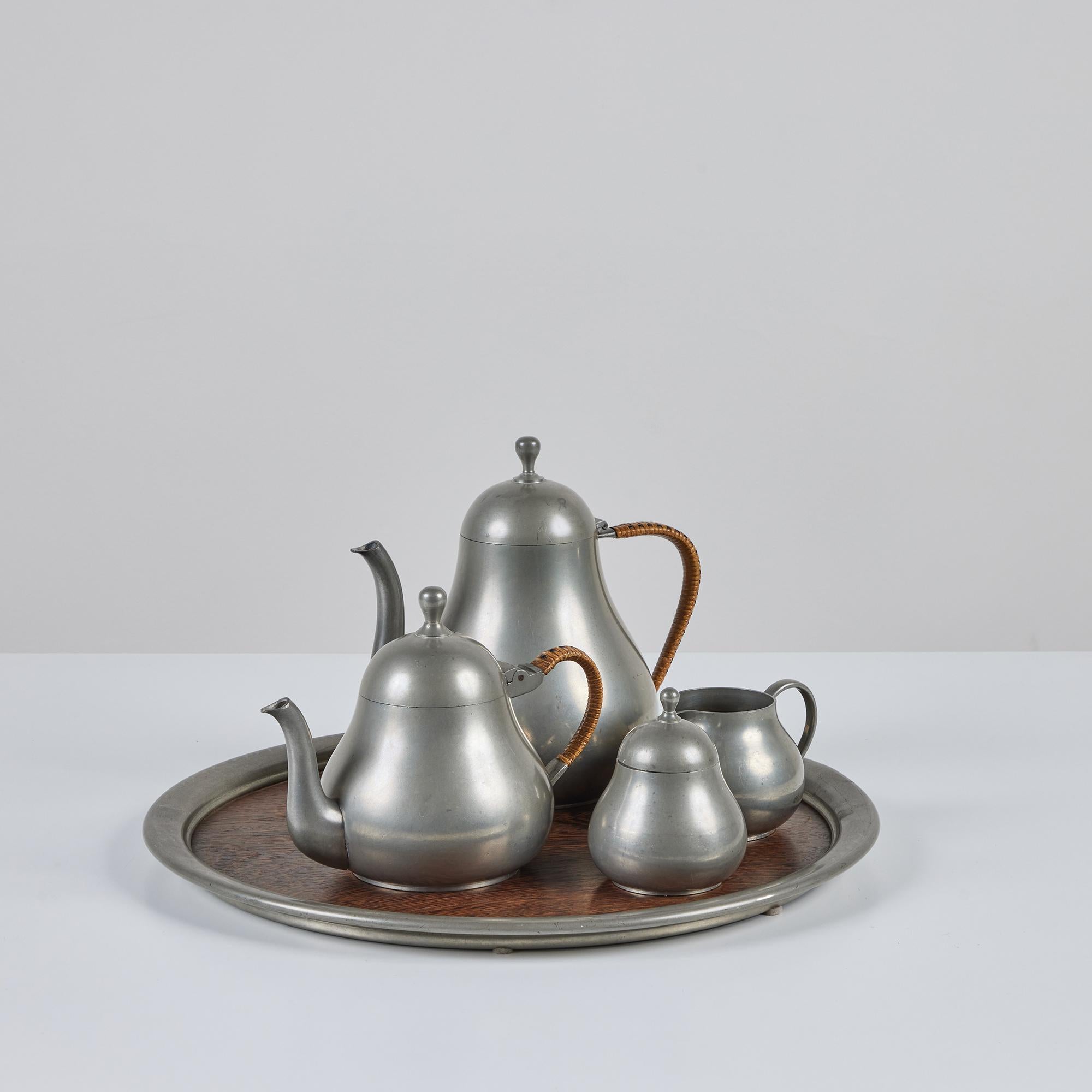 Meeuws & Zoon Den Haag five-piece service set in pewter with woven handles on both the coffee and tea pot. This Netherlands pewter set consists of one lidded coffee pot, one lidded tea pot, one creamer, one lidded sugar vessel, and a serving tray.