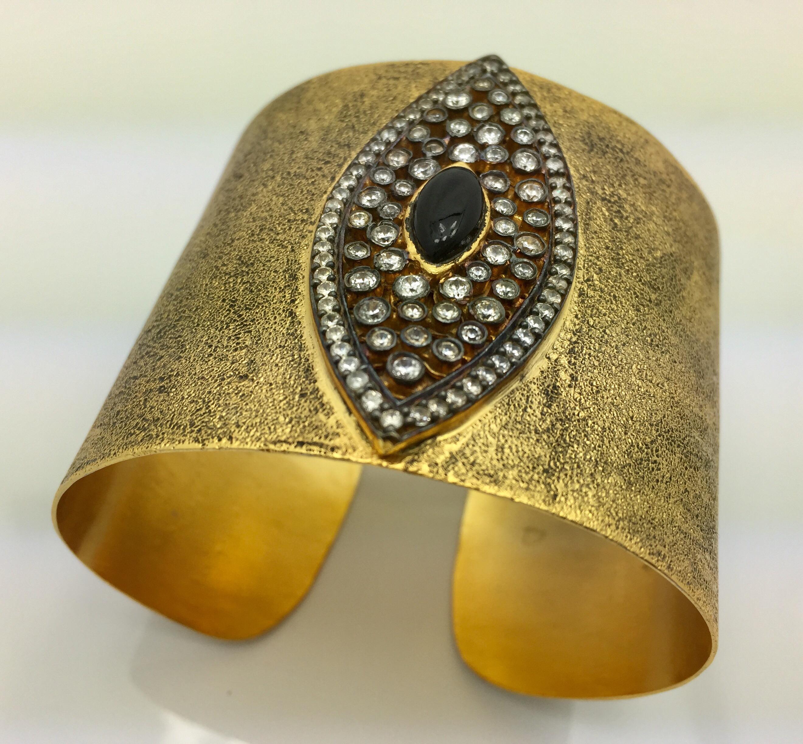 The evil eye, thought to provide protection from evil spirits is beautifully captured in this gold, black and CZ hand brushed cuff. The statement cuff is lavishly adorned with sparkling CZ stones.  Cuff is adjustable. Only 1 available.

Measures