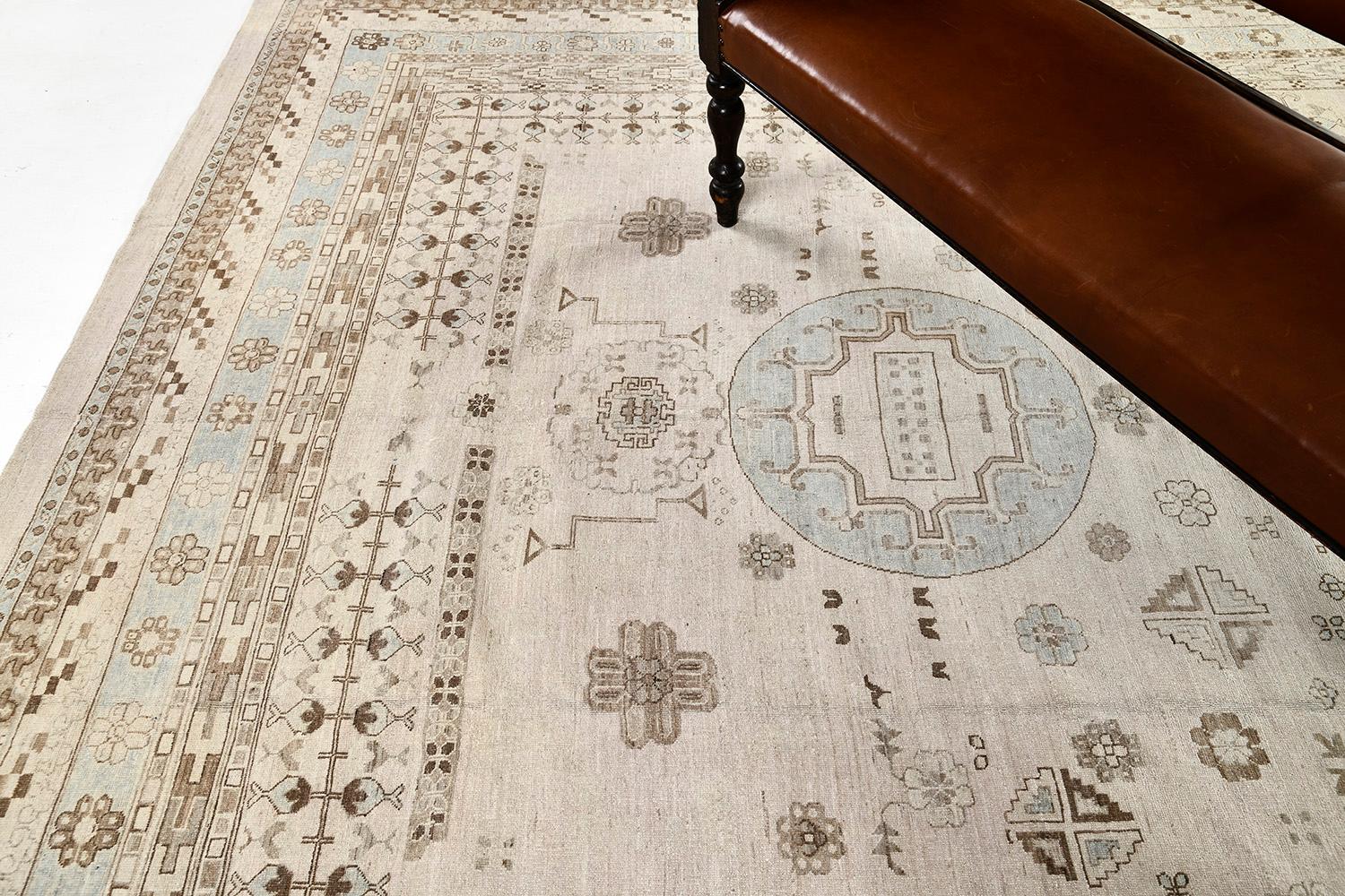 A classy revival of hand-spun wool from our collection of Khotan Rug lit the strong points of contrast of muted tones of blue and beige. Three majestic medallions are aligned that have spaces at the center filled with varying geometric elements and