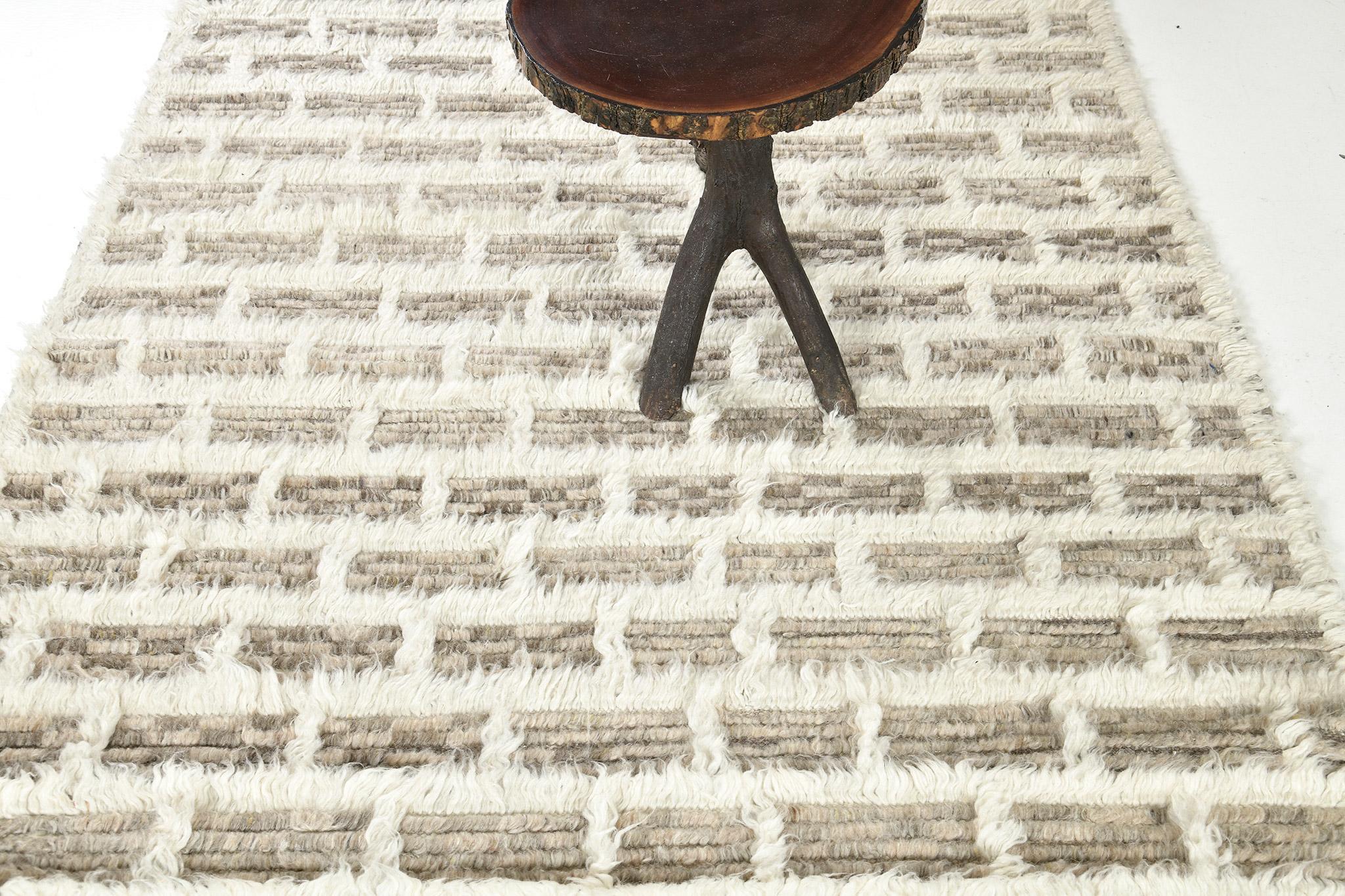 In the Ahina rug, a rectangular grid frames a field of dappled pile tones. This piece combines ivory lines with heathered clay and taupe tones. 

Hand knotted of hand-spun wool, the Sahara Collection melds linear organization with a relaxed organic