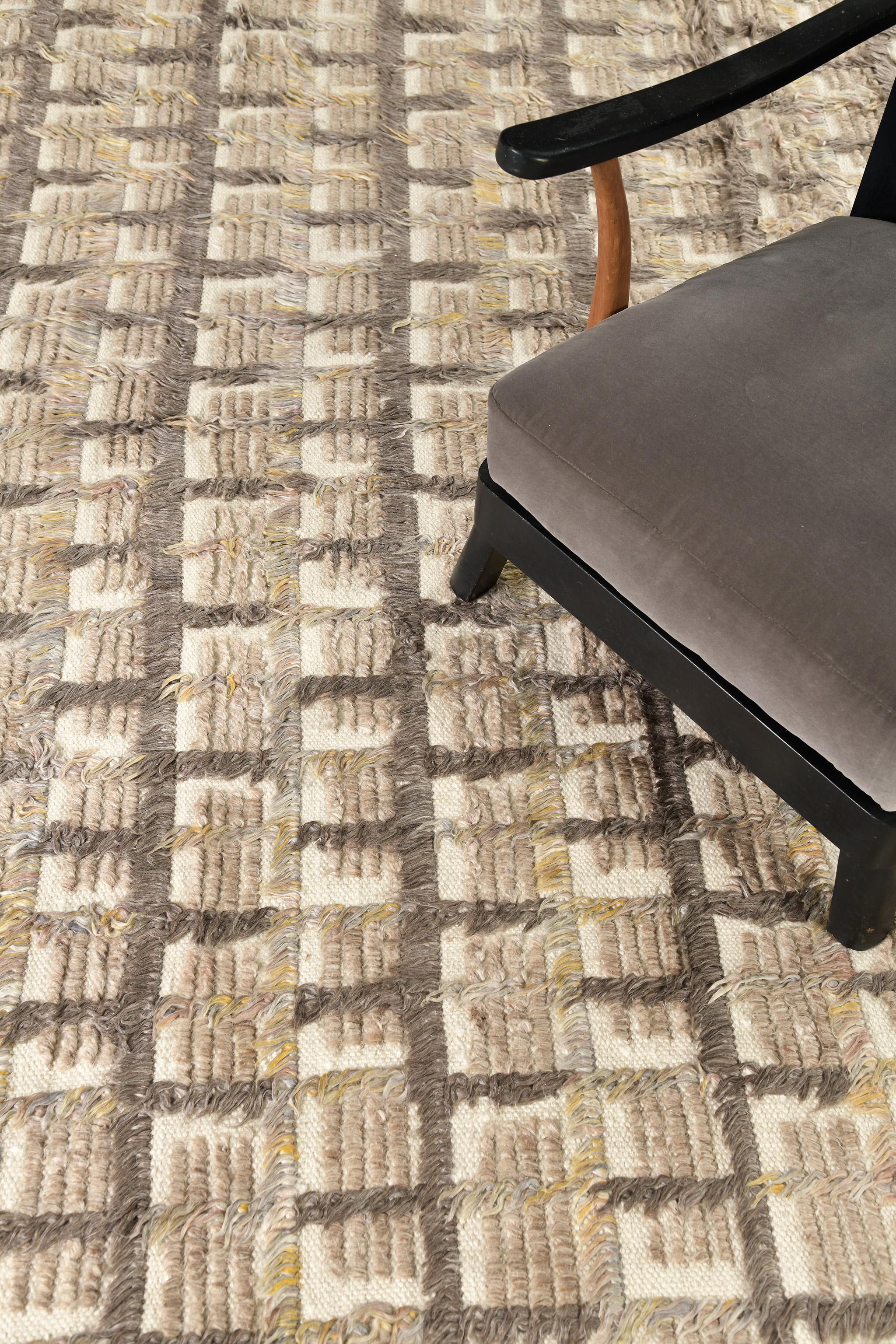 The Hanin rug is a complex multi-toned grid motif in long pile lines with shapes of trim pile, and open flatweave accents. Texturally rich with tonal dimensional effects, Hanin is rendered in a warm mix of cacao, clay and gold inflected mixed gray