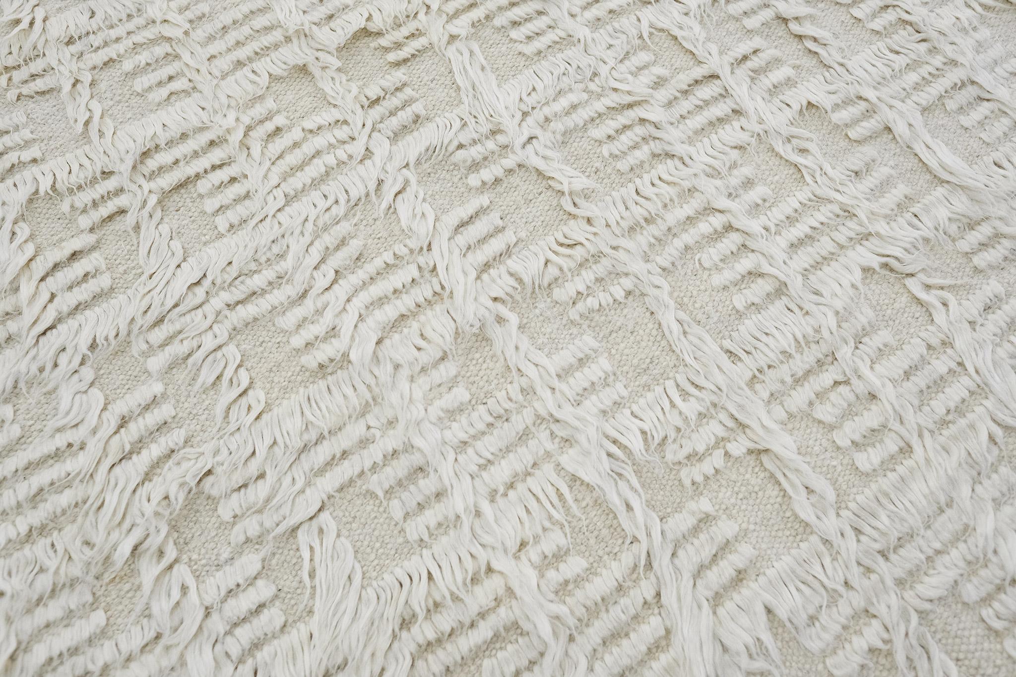 Der Teppich Mani ist ein monochromes Design, bei dem sich Lang- und Kurzflor mit offenem Flachgewebe abwechseln. Dieses Stück ist aus elfenbeinfarbener Naturwolle gefertigt.

Die Sahara-Kollektion, eine Erweiterung des beliebten Amihan-Designs von